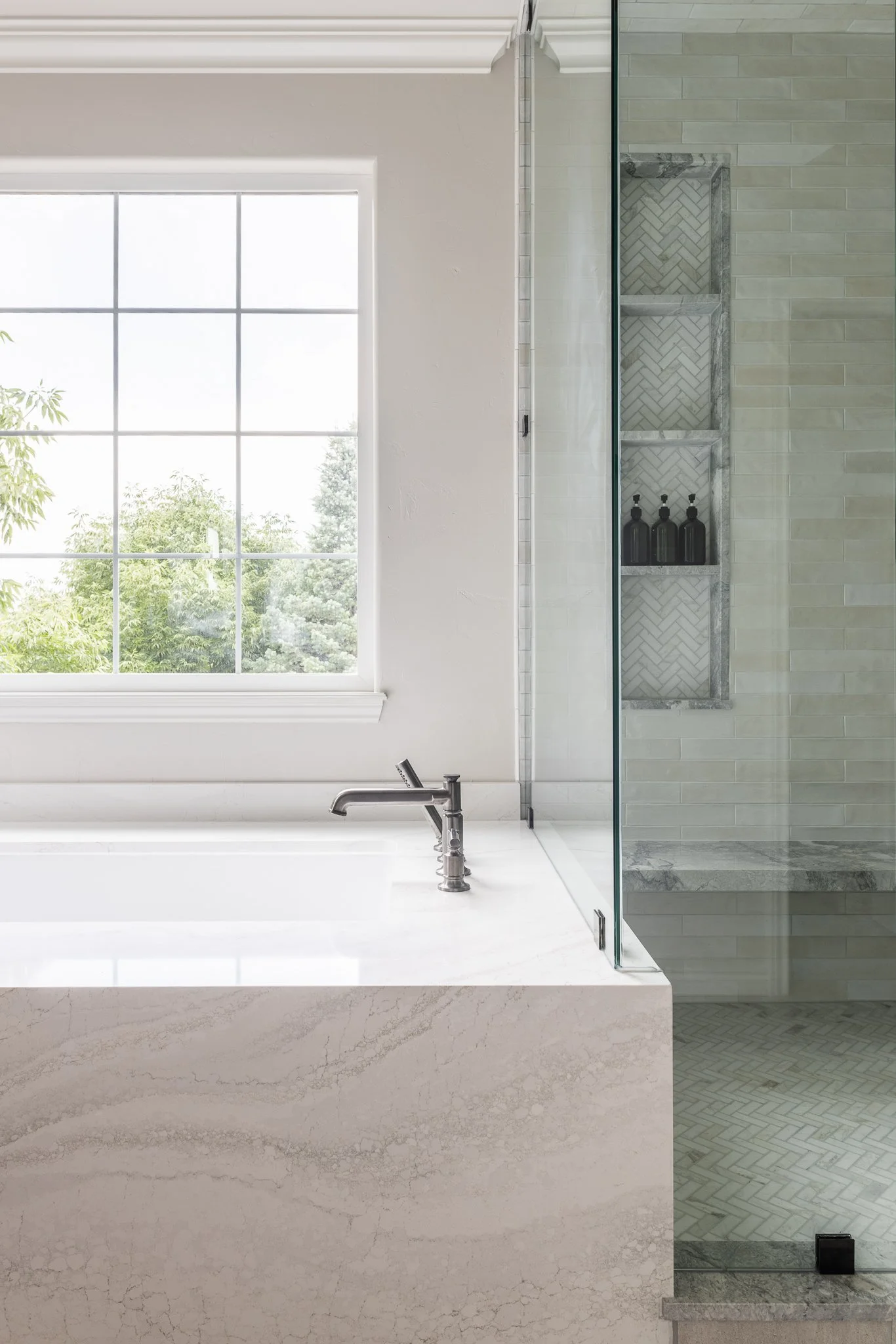 Modern bathroom interior with large window, marble bathtub, and glass-enclosed shower with built-in shelving.