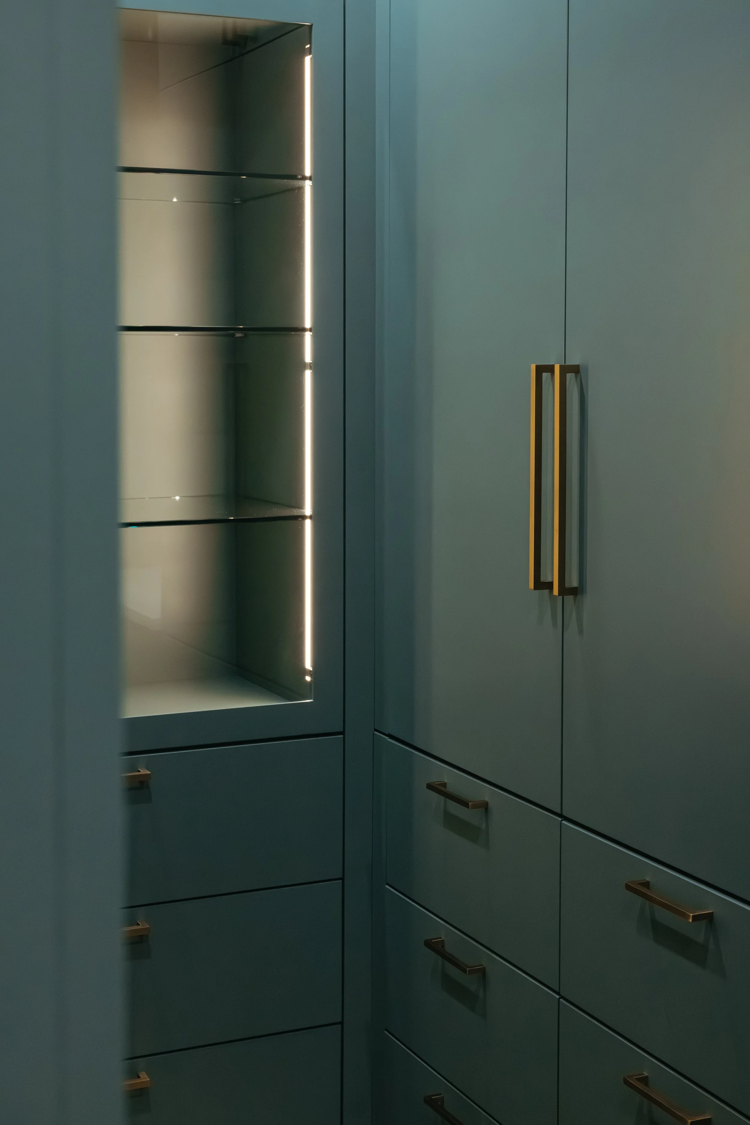Modern closet with blue cabinetry, glass shelves, and bronze handles.