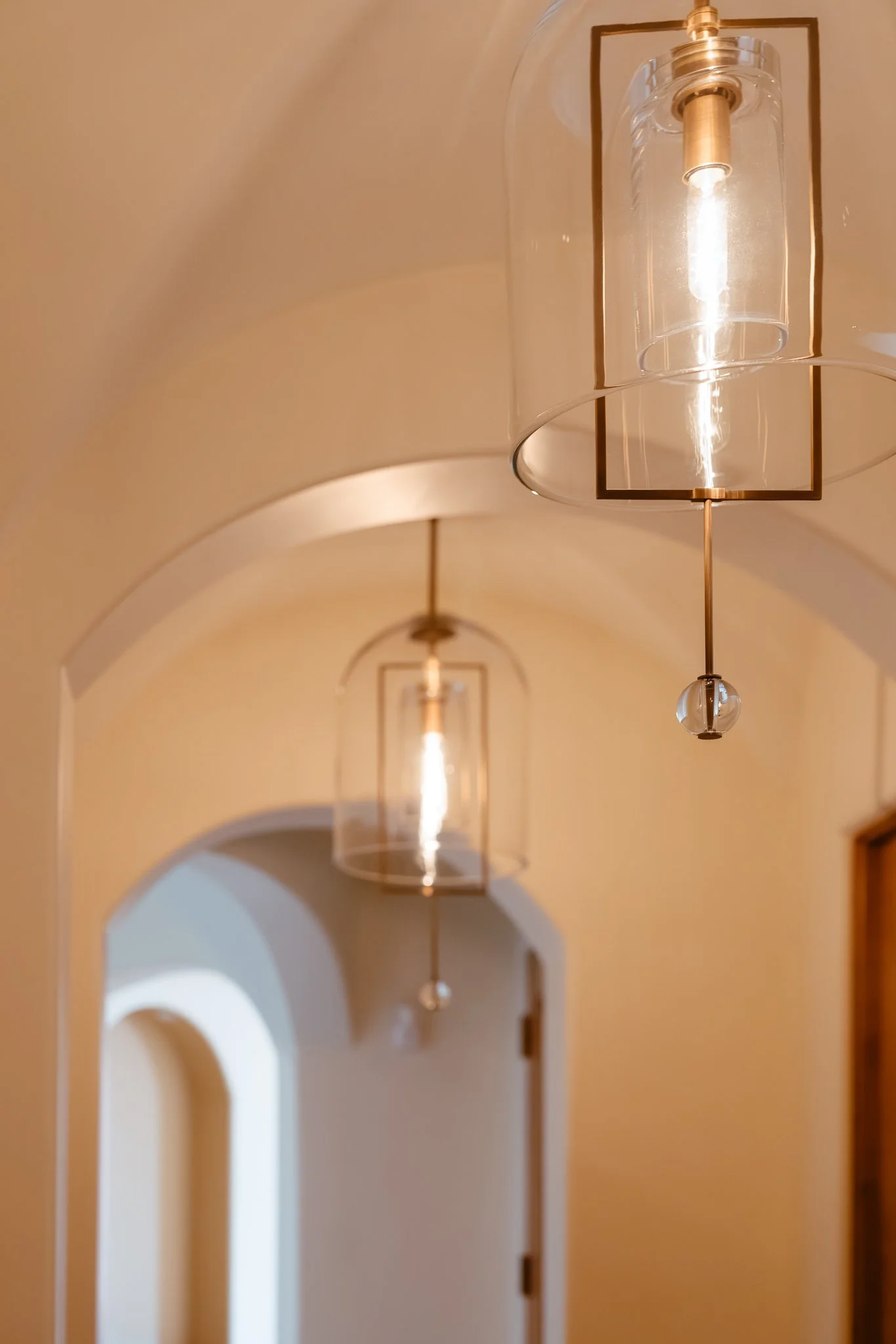 Modern pendant lights hanging in a hallway with arched doorways and beige walls.
