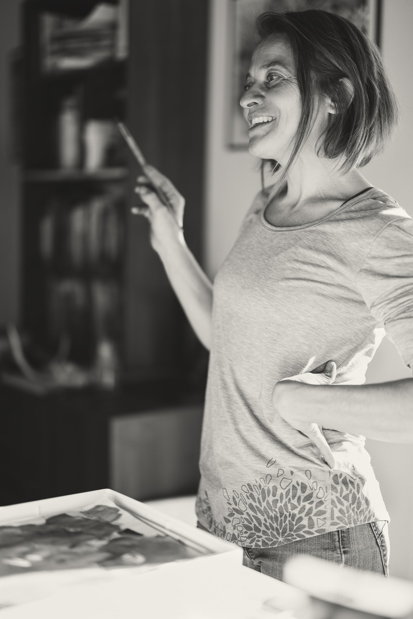 Black and white image of a smiling woman holding a smartphone in a casual indoor setting.