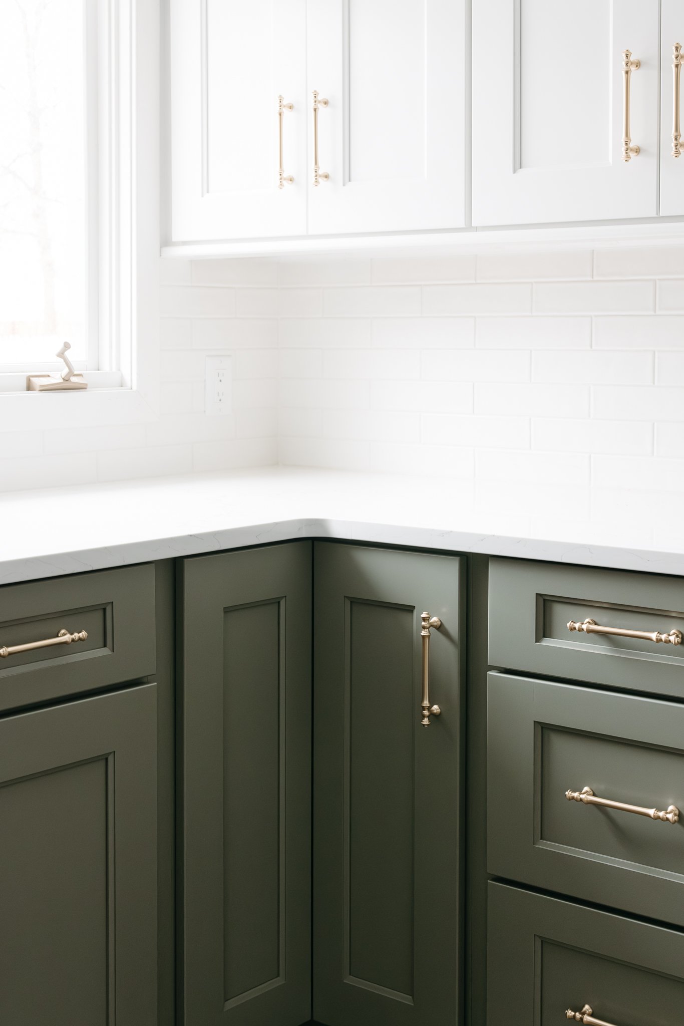 Modern kitchen corner with white upper cabinets, green lower cabinets, gold handles, and white subway tile backsplash.