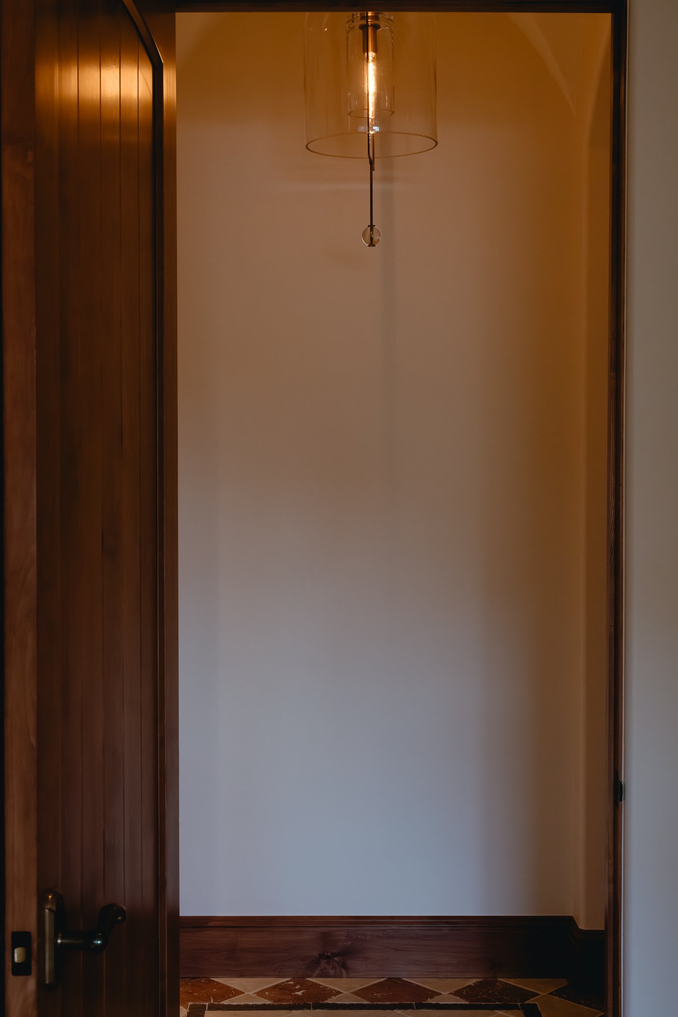 Interior hallway with a wooden door, white walls, and a pendant light fixture.