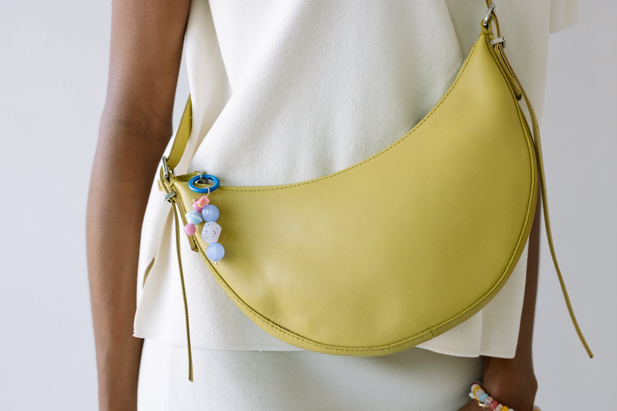 Person wearing a yellow crescent-shaped handbag with colorful beads attached, over a white outfit.