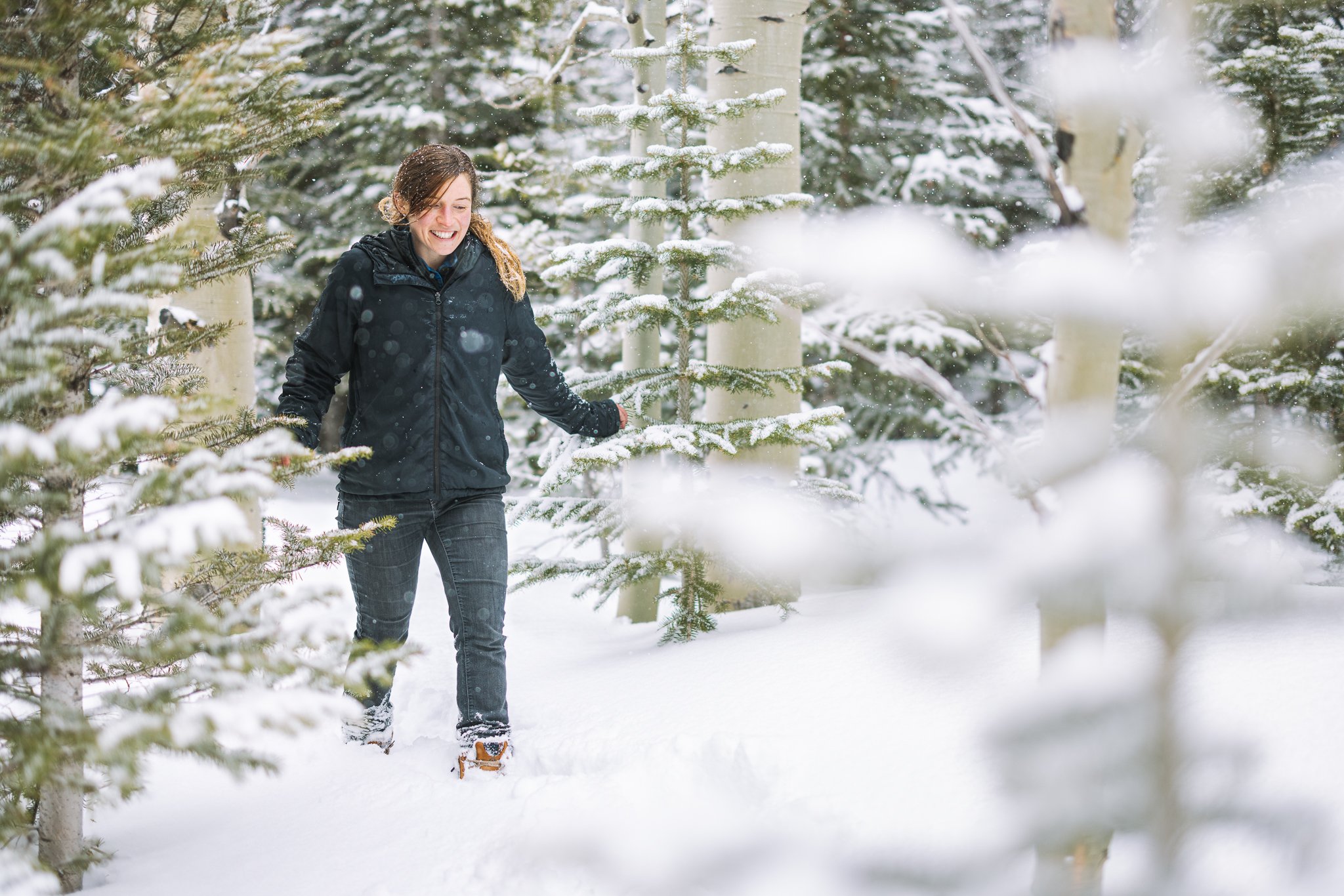 Woman walking through a snowy forest, wearing winter clothing.