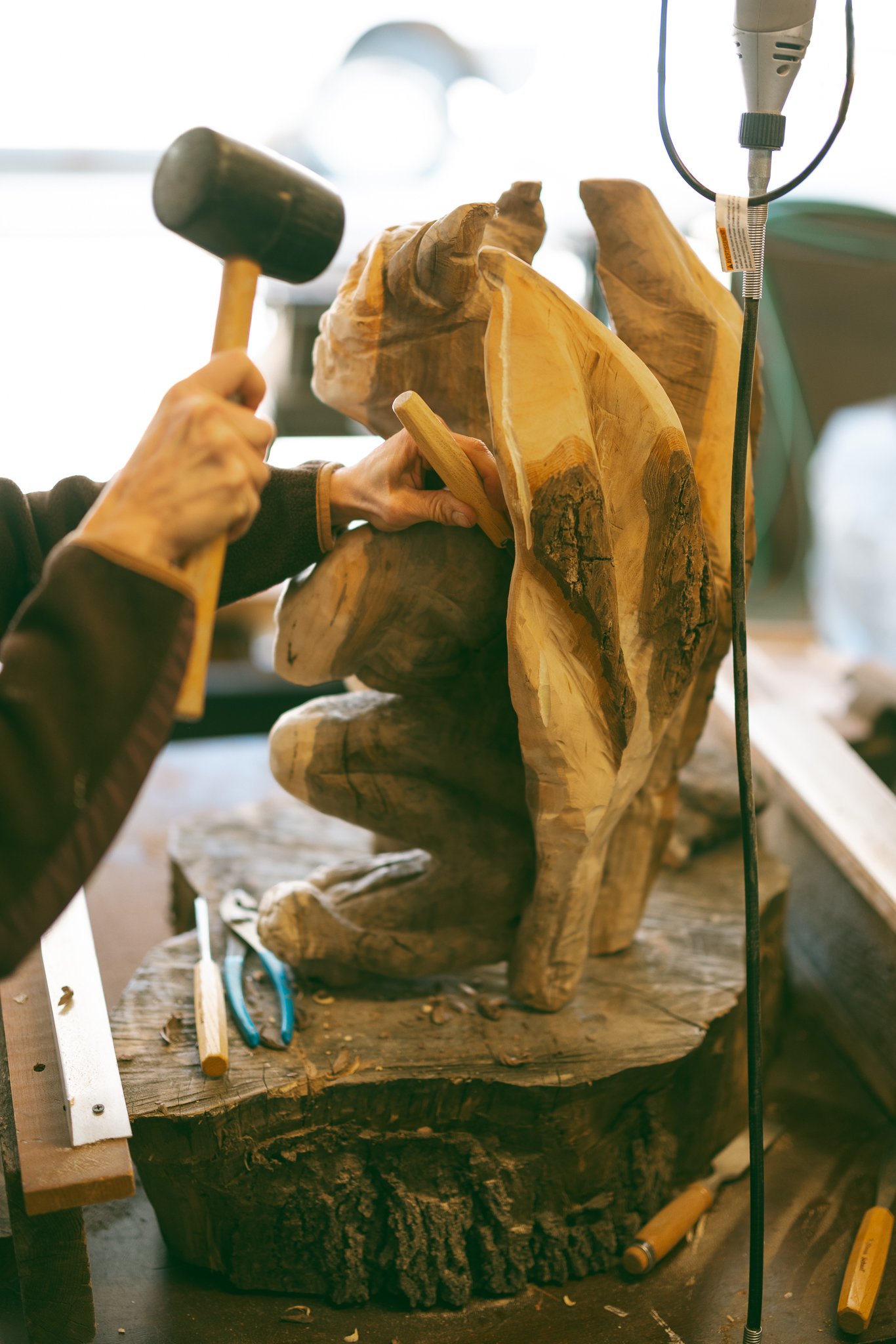 Artist carving wood sculpture with mallet and chisel, surrounded by tools