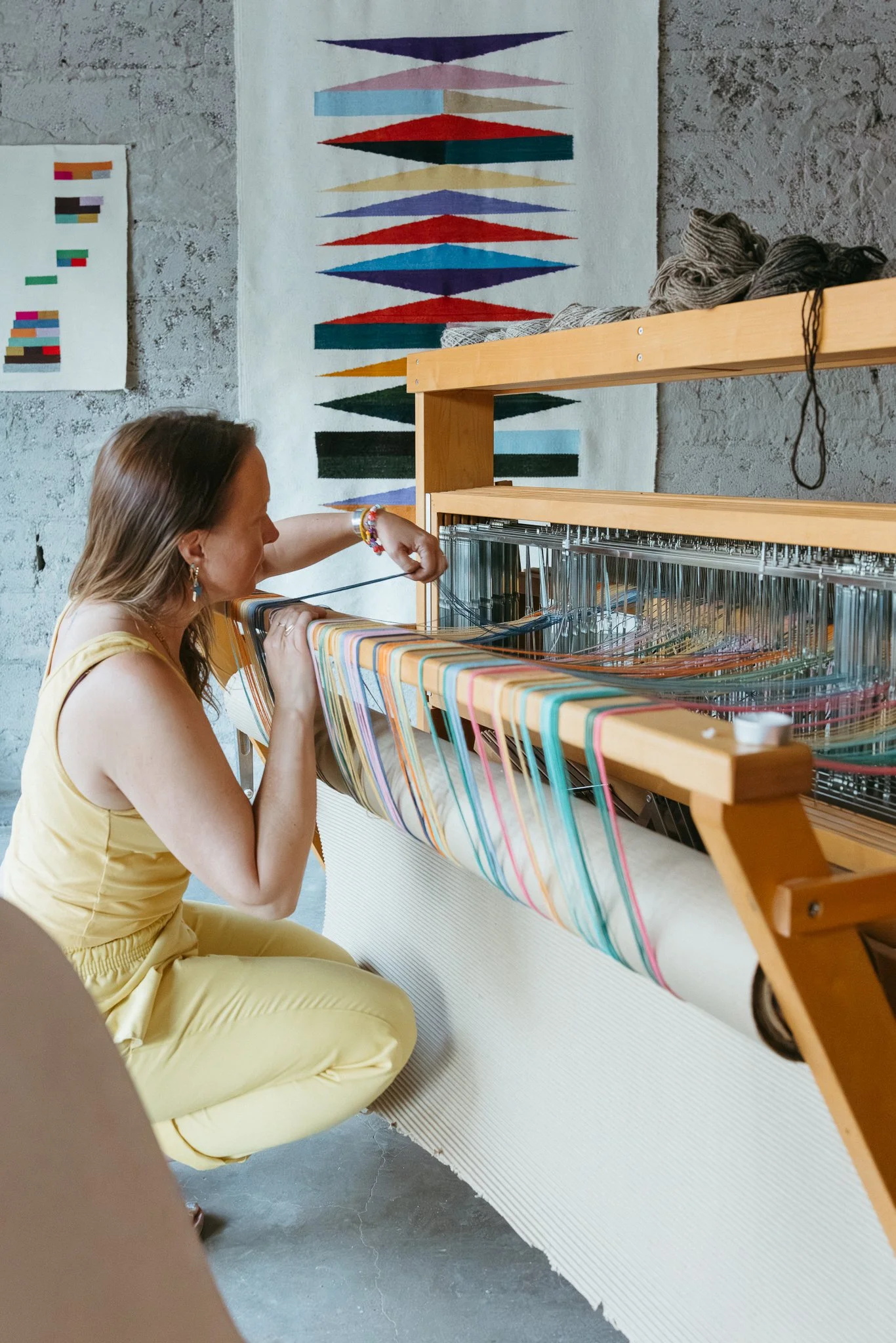 Textile artist weaving colorful threads on a loom in a bright studio environment