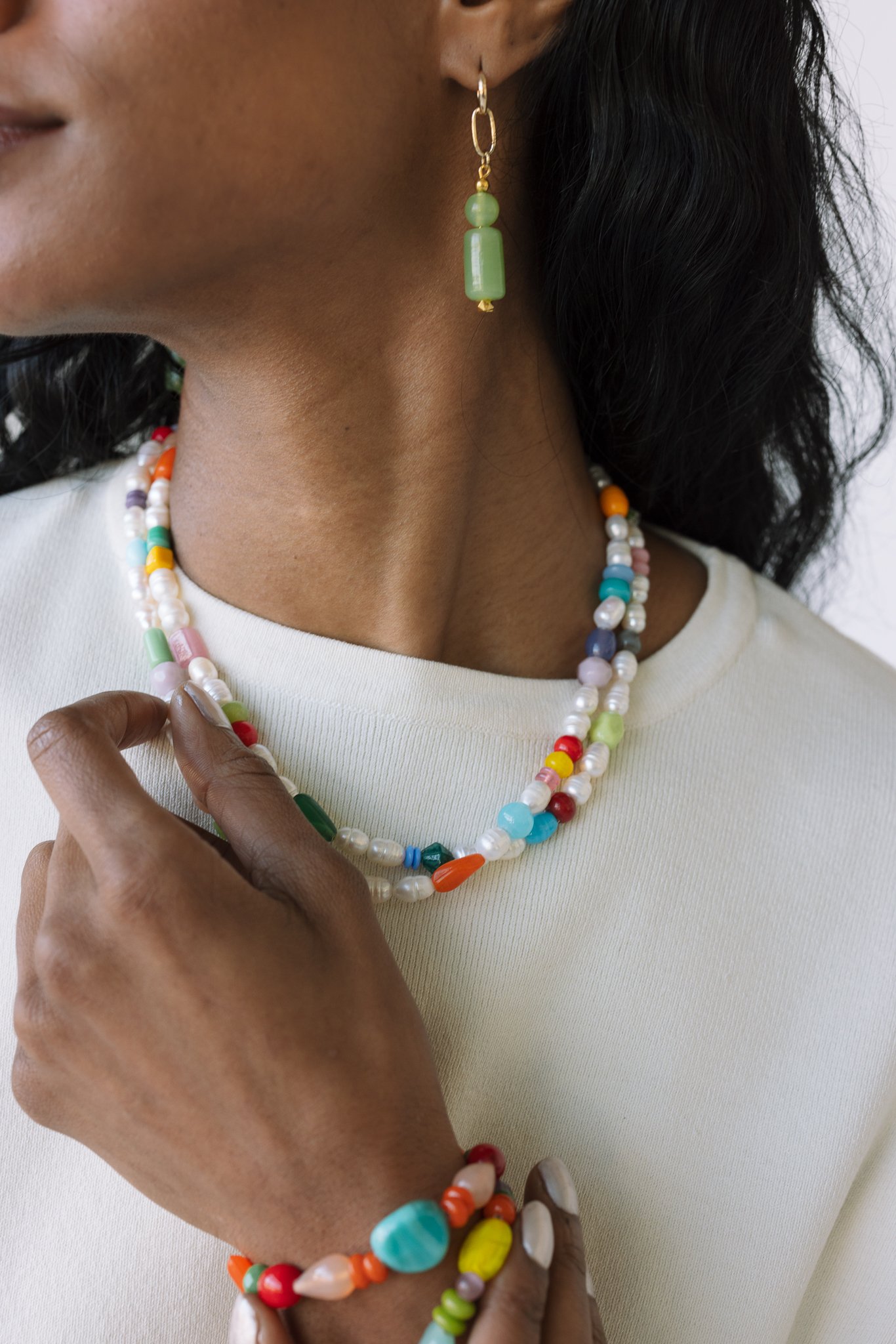 A person wearing colorful beaded jewelry, including a necklace, bracelet, and earring, over a light-colored top.