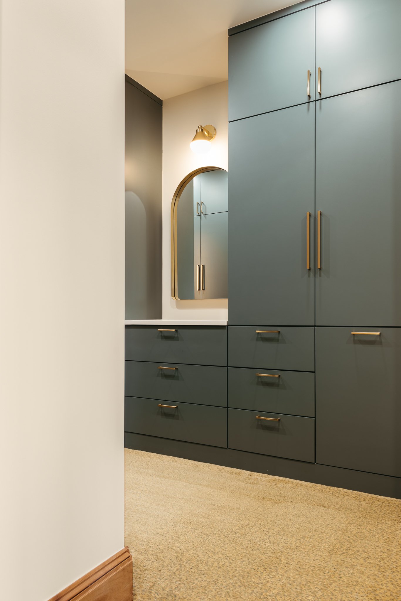 Interior of a modern closet with green cabinets, gold handles, an arched mirror, and a light fixture.
