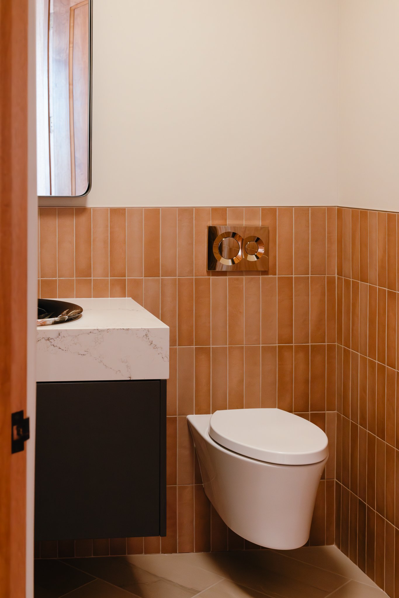 Modern bathroom with wall-mounted toilet, beige and brown tiles, countertop sink, and wall mirror.