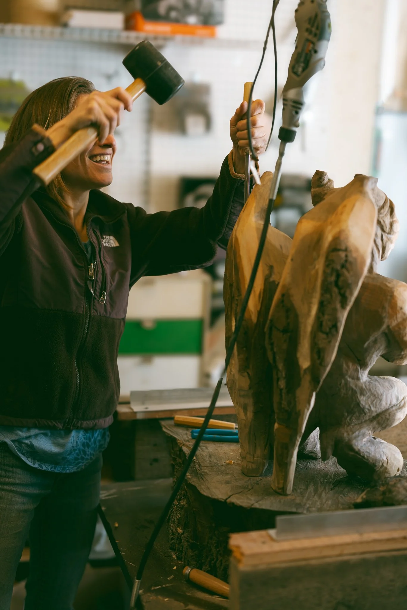Artist carving a wooden sculpture with hand tools in a workshop, captured as an environmental portrait