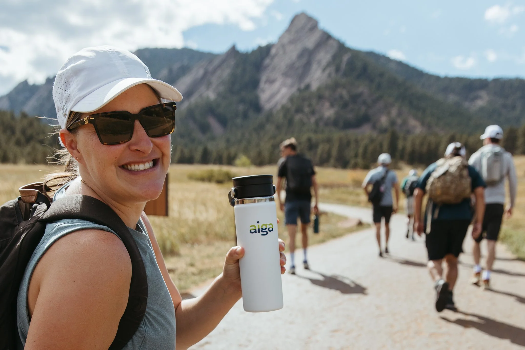 Woman with sunglasses and a drink with attendees gathered outdoors during the AIGA Colorado retreat, photographed in a natural mountain setting.