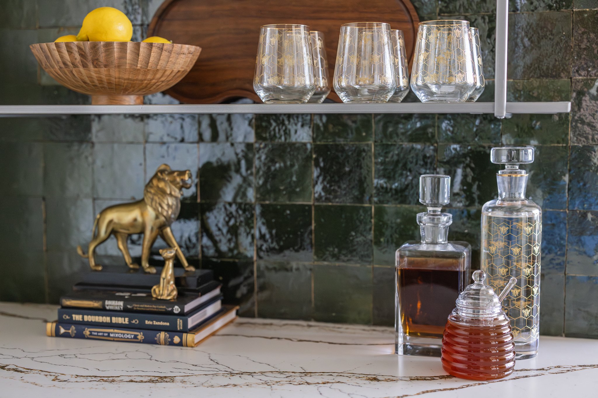 Stylish bar setup with decanters, glasses, a wooden bowl of lemons, lion statue, and colorful tiles.