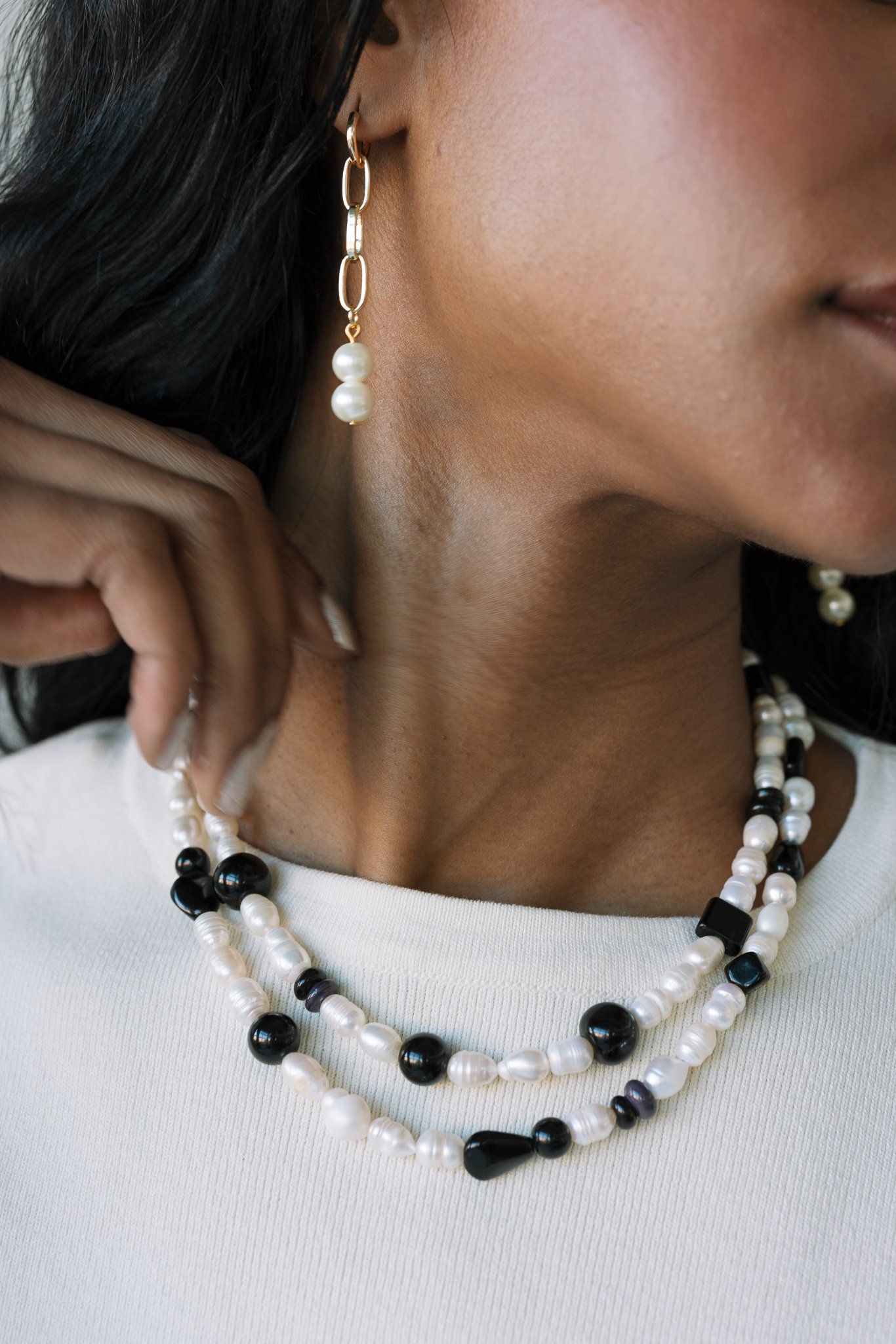Person wearing earrings and a pearl necklace with black beads on a white shirt.