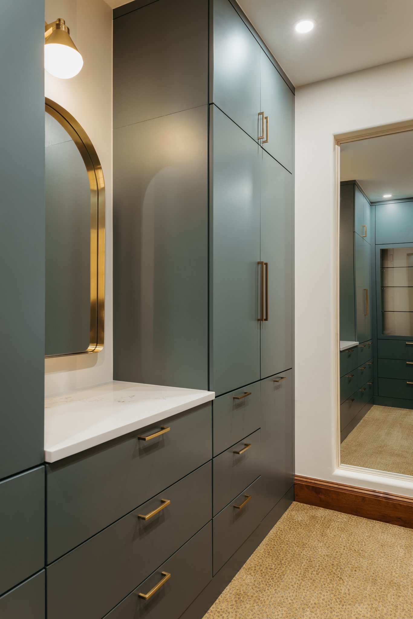 Modern walk-in closet interior with teal cabinets, gold handles, built-in vanity, and a large mirror.