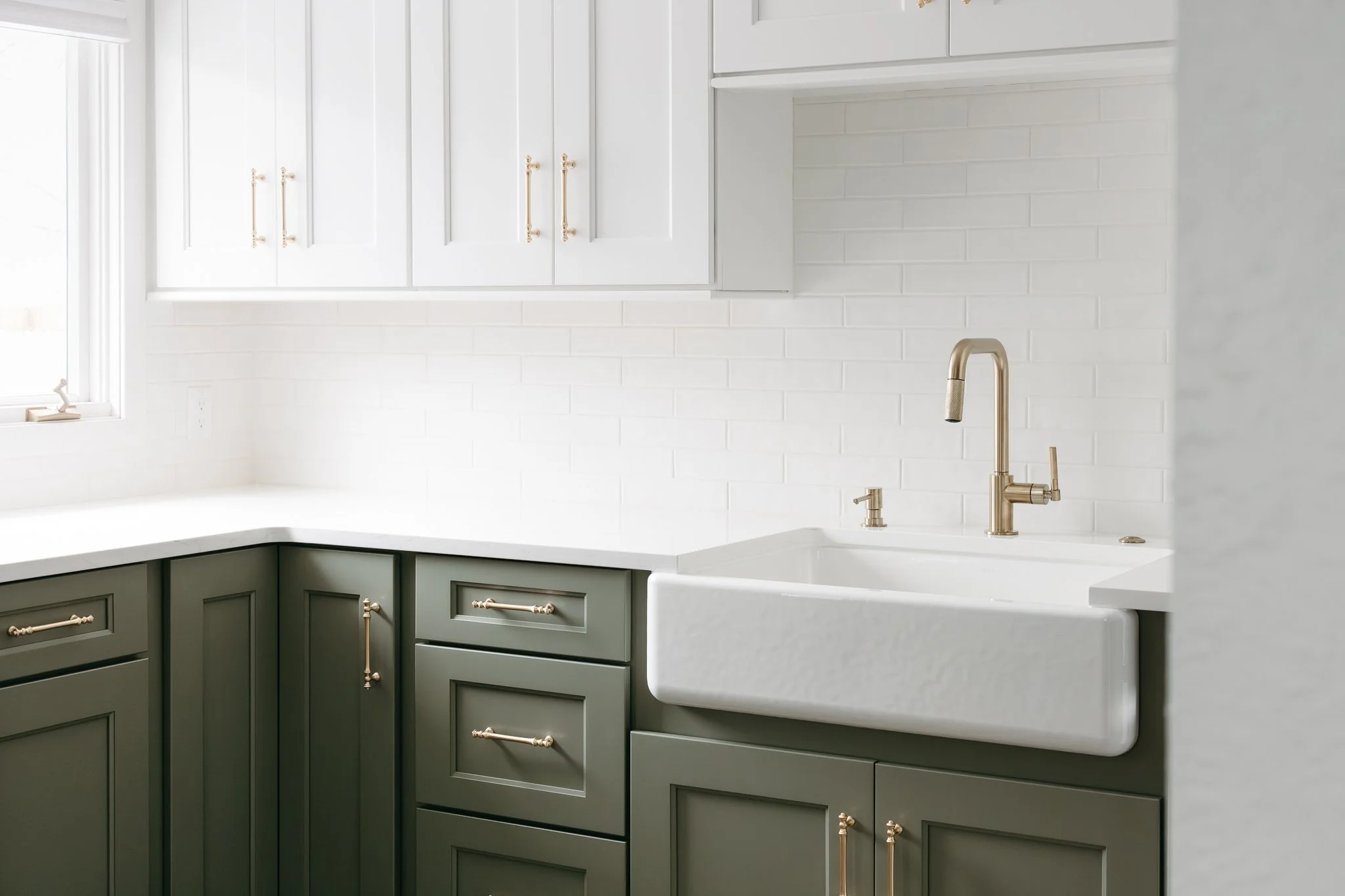 Modern kitchen corner with green cabinetry, white farmhouse sink, and brass faucet.