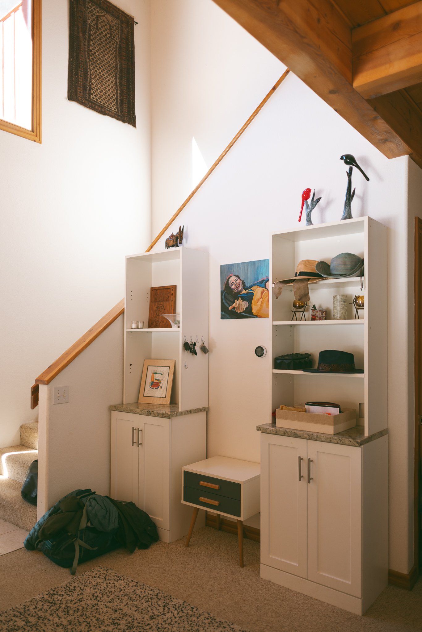 Interior scene with two white cabinets, decorative items, a wall painting, and a small table under a staircase.