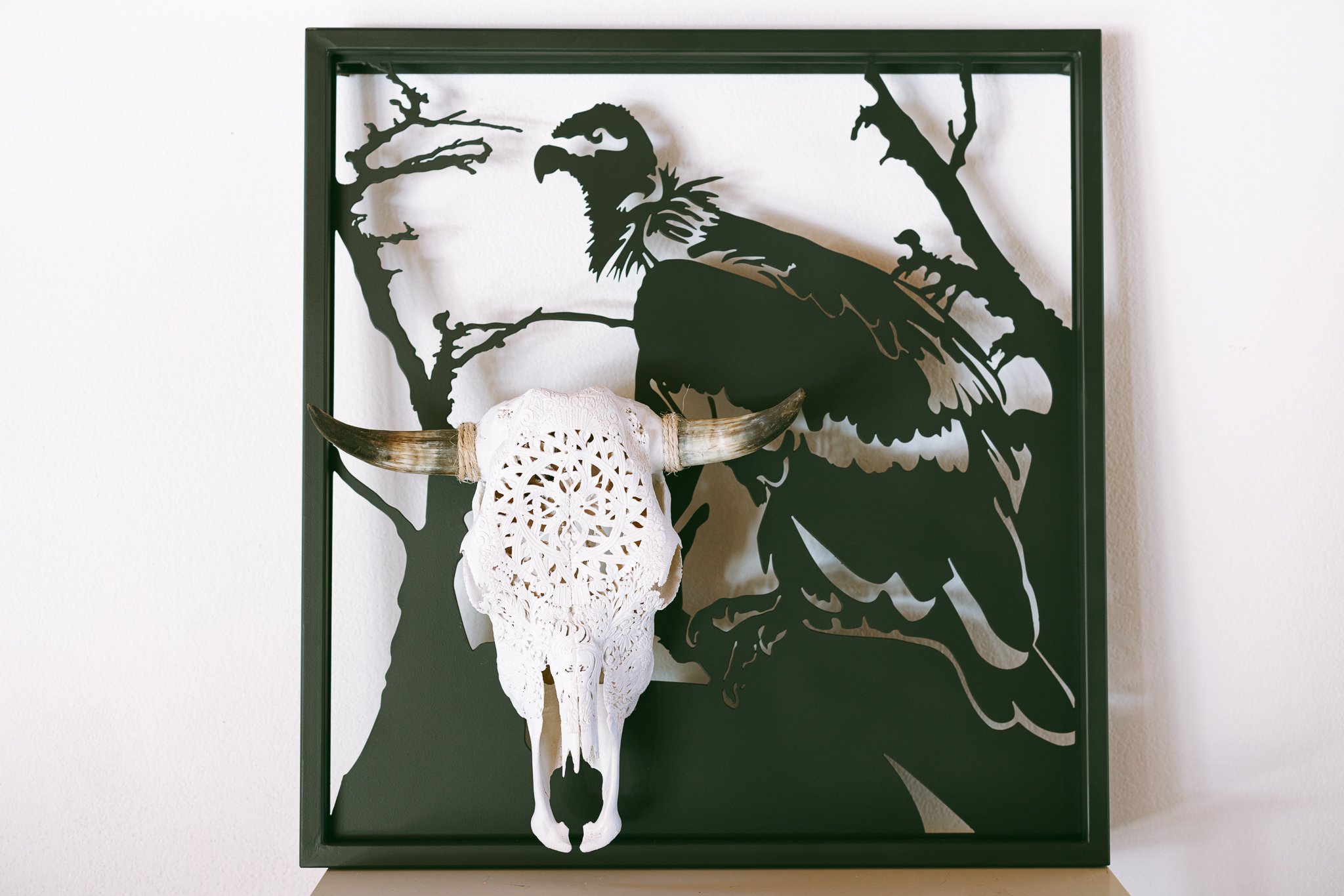 Decorative buffalo skull with lace overlay and metal vulture silhouette in black frame.