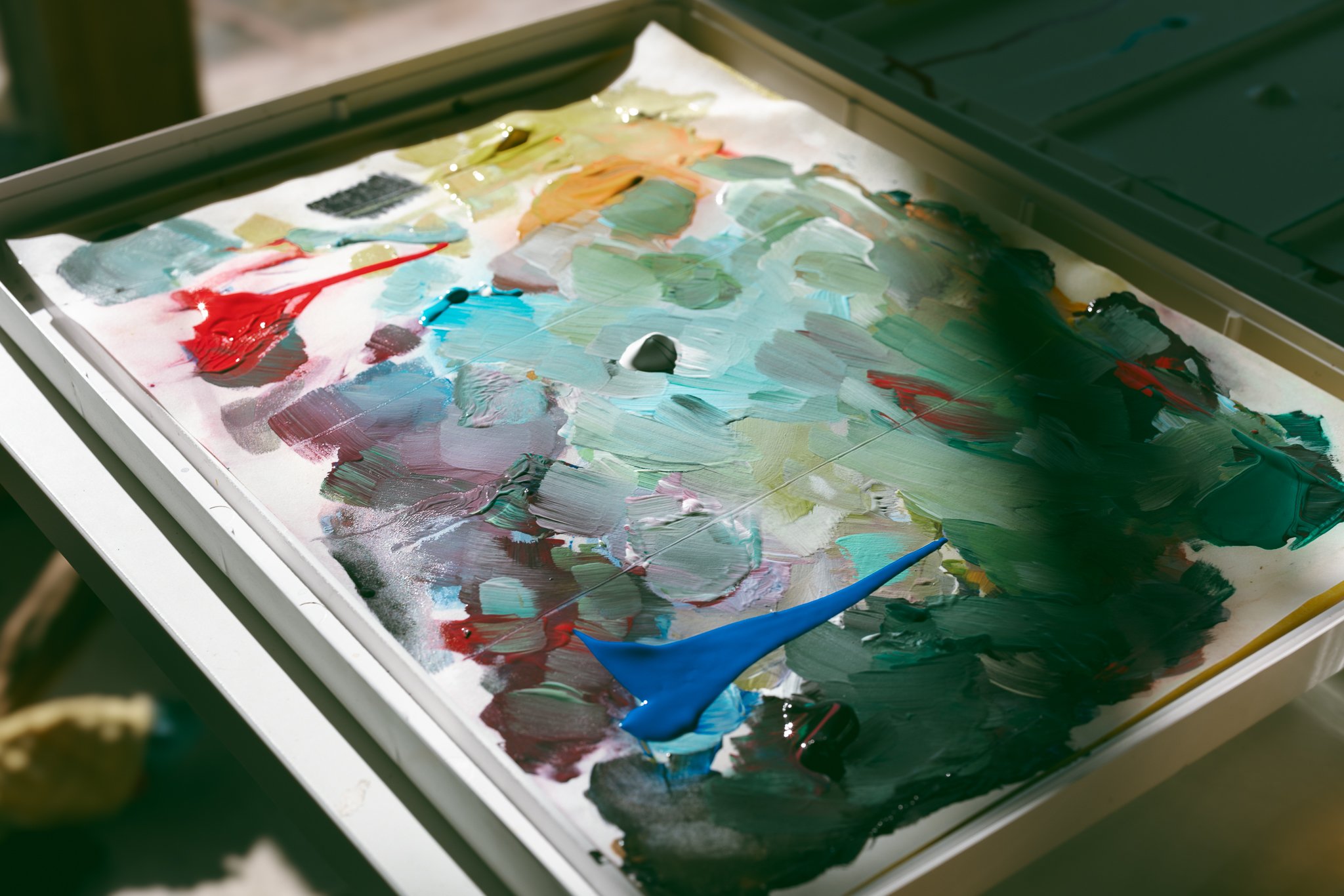 Mix of colorful paint blobs on an artist's palette in sunlight.