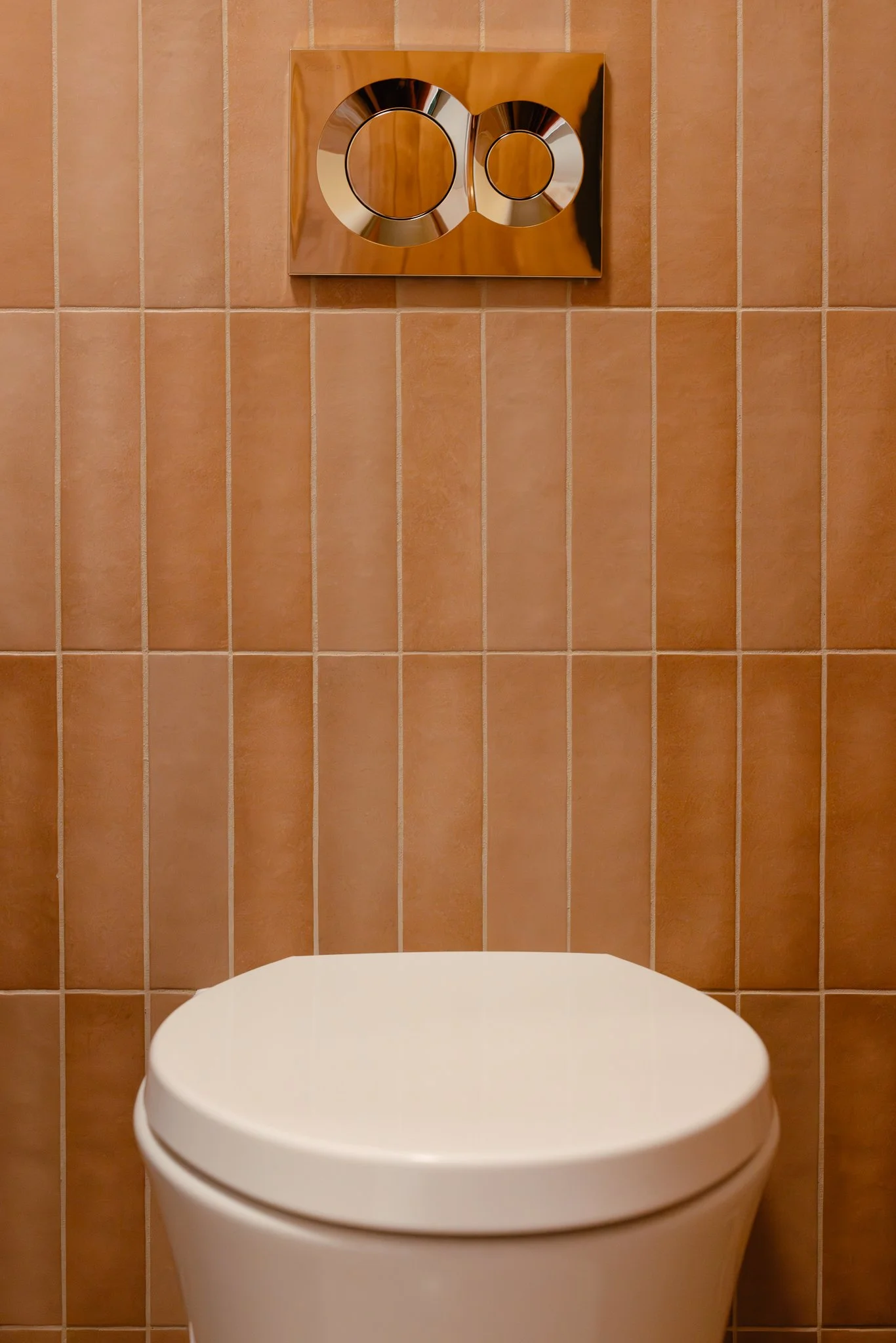 Toilet with a beige tiled wall and dual flush button