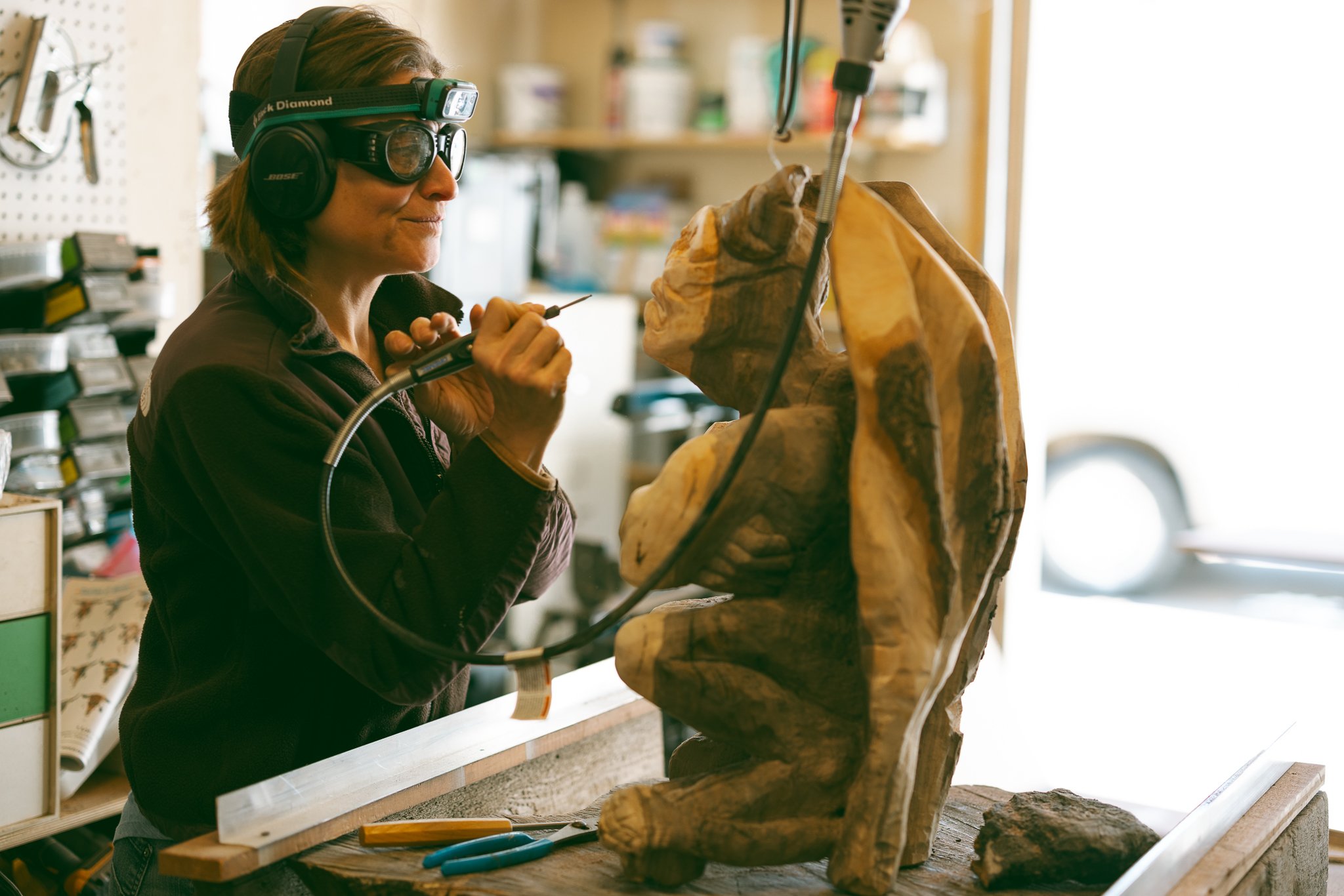 A person wearing safety gear carving a wooden statue in a workshop