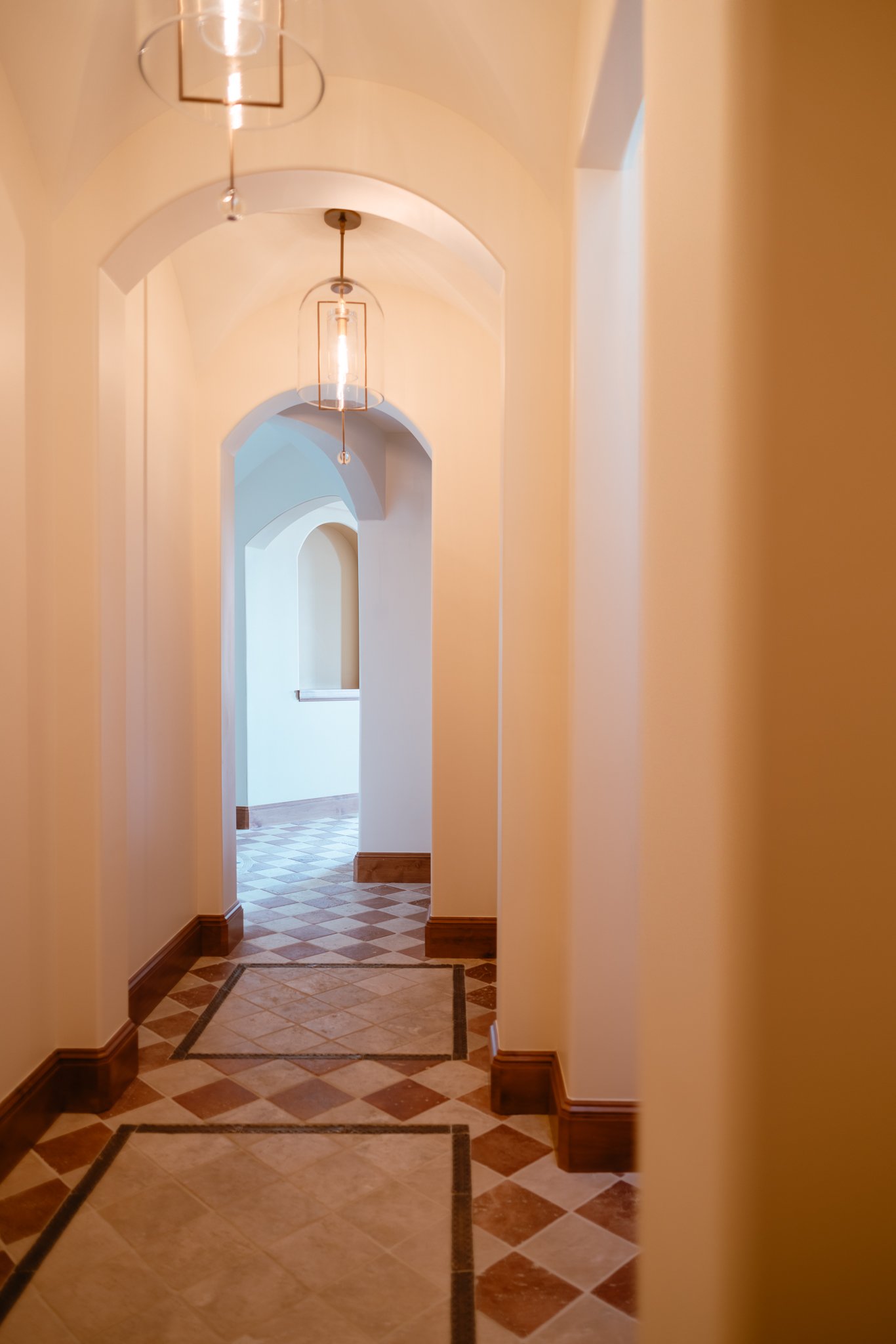 Elegant hallway with arched doorways and pendant lighting, featuring tiled flooring and soft beige walls.