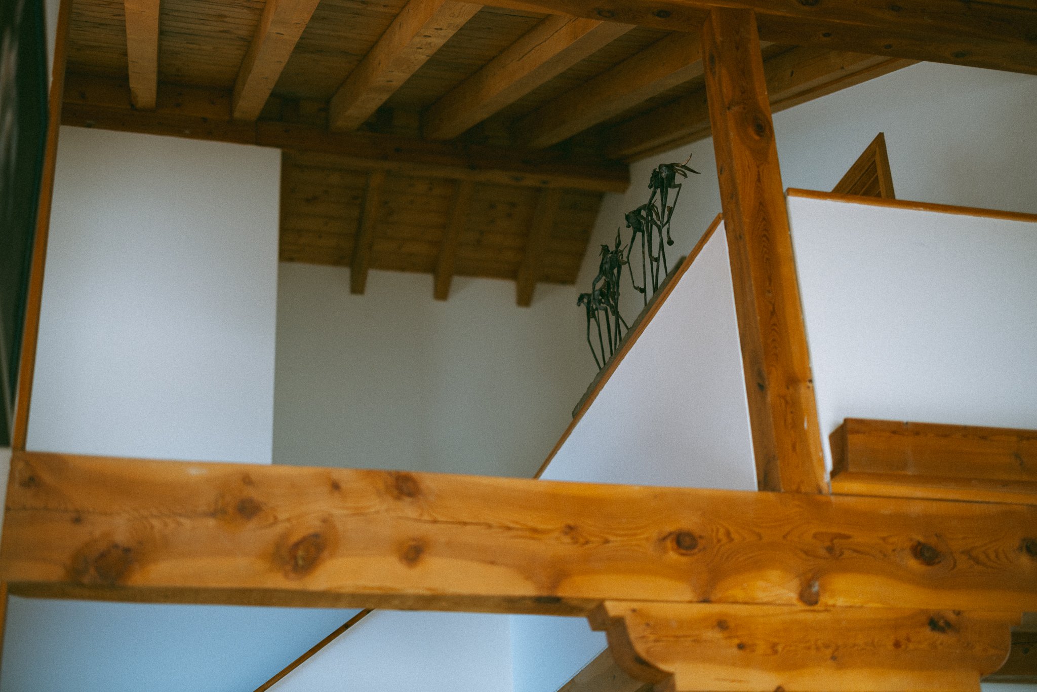 Interior with wooden beams and white walls, featuring a staircase and sculptures.