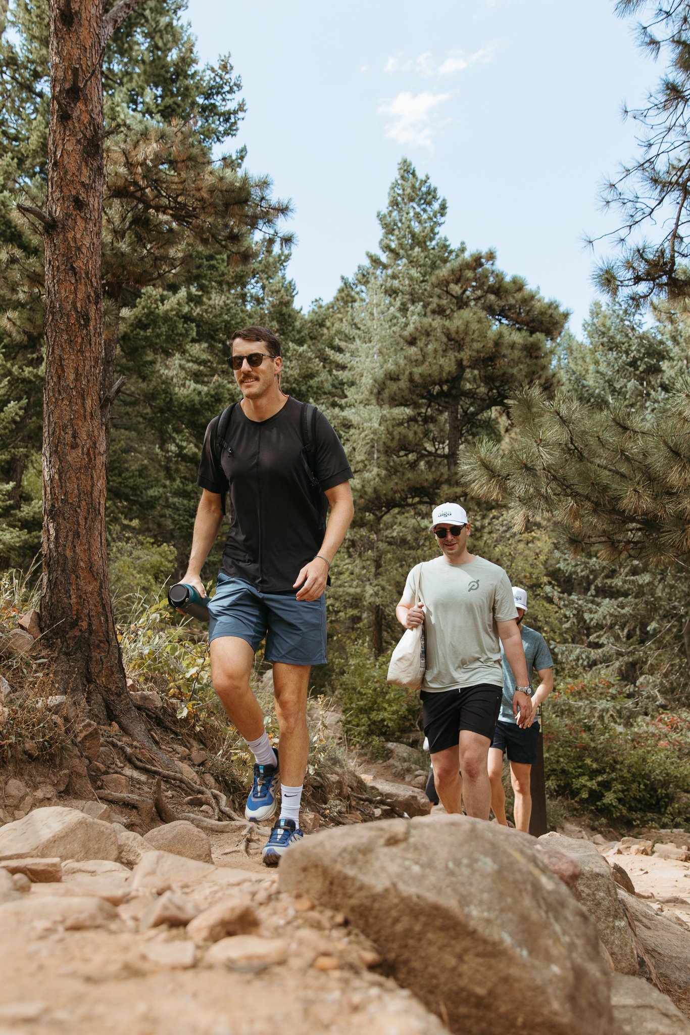 Group of people hiking on a rocky trail surrounded by pine trees under a clear sky.
