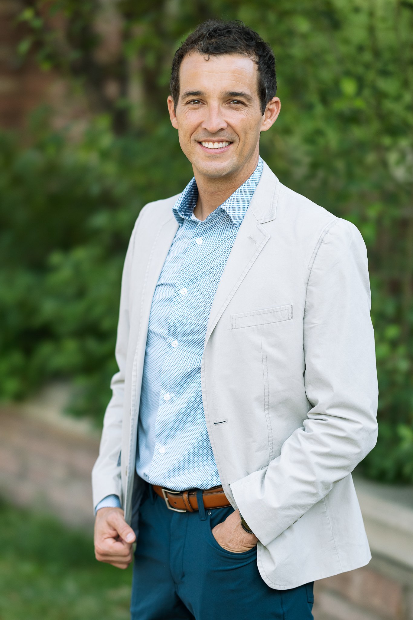 Man in light gray blazer and blue shirt smiling outdoors