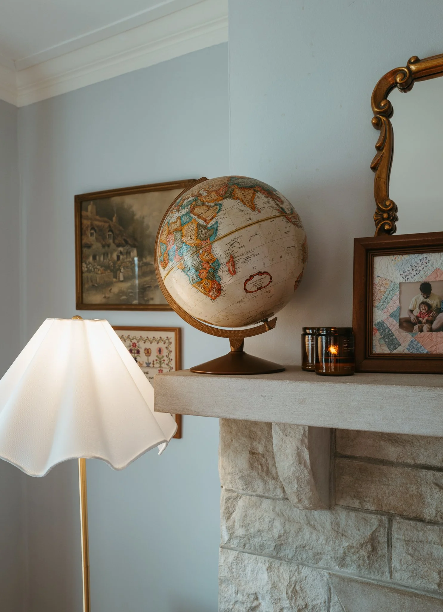 Styled fireplace mantel with vintage globe, framed artwork and table lamp, showcasing curated decor and warm interior design details