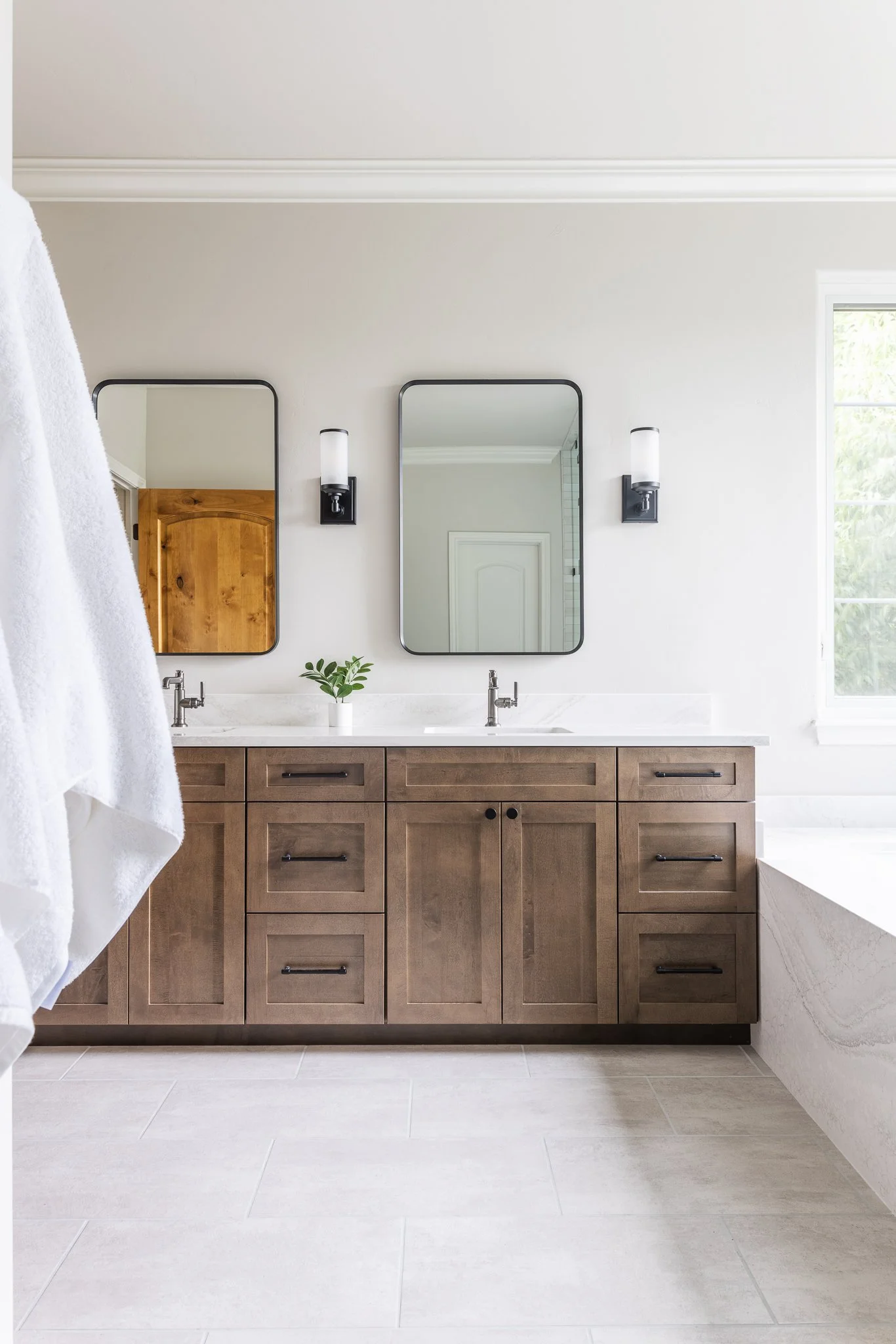 Modern bathroom with double vanity, two mirrors, wooden cabinets, and wall sconces.