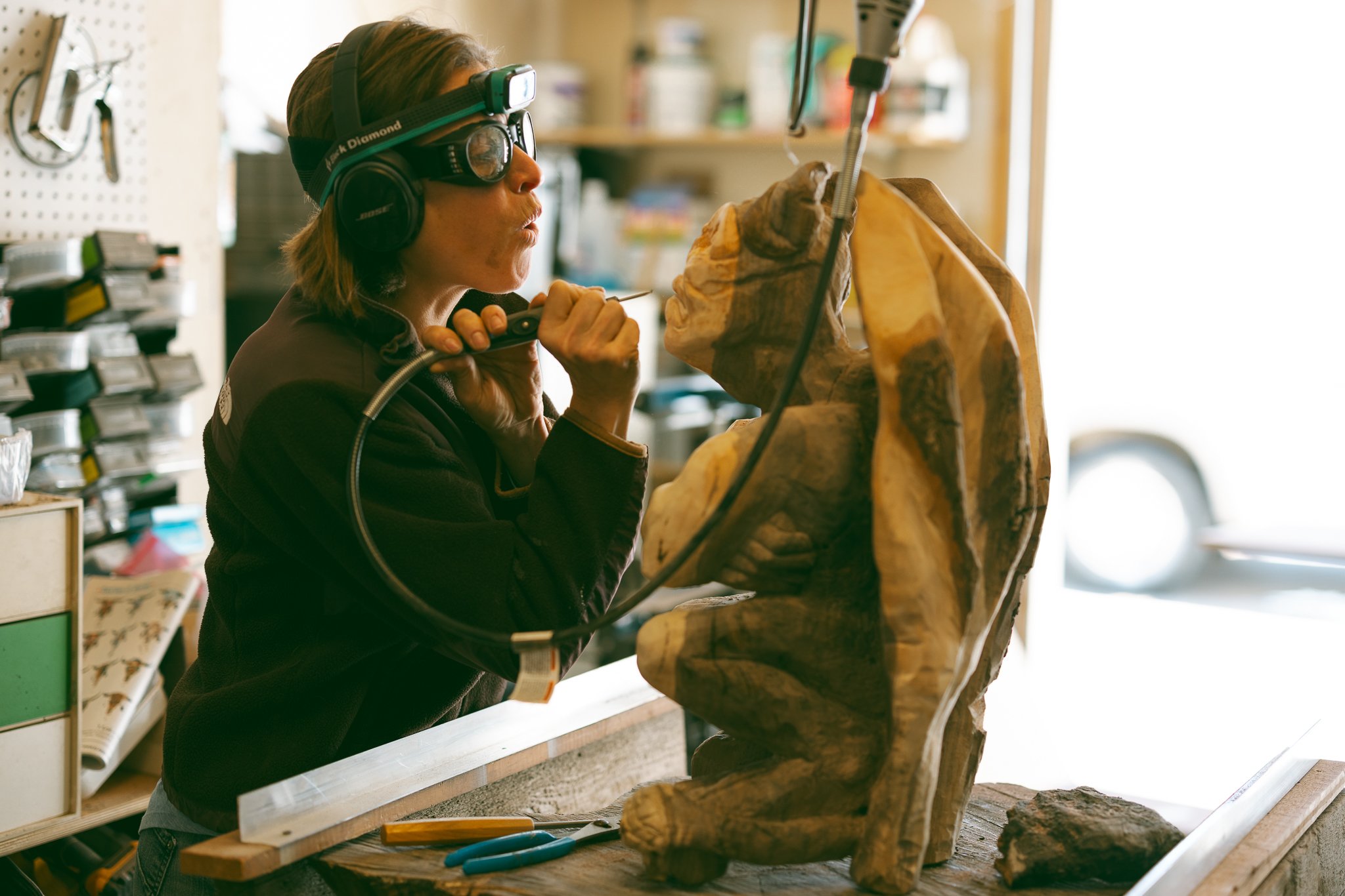 A person using carving tools to sculpt a wooden figure in a workshop.