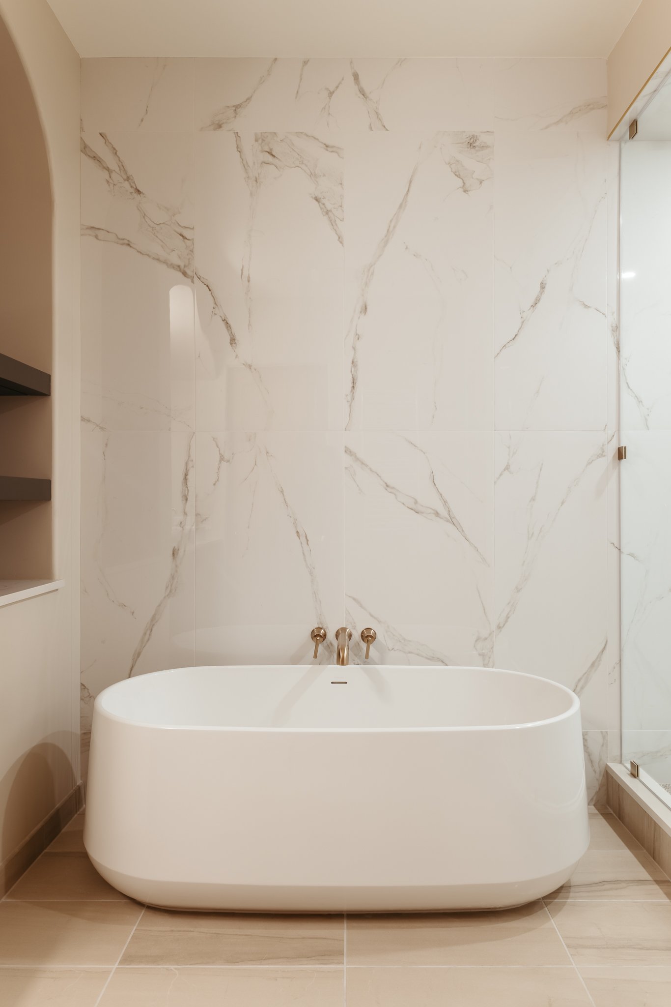 Modern bathroom with freestanding white bathtub, marble wall tiles, and gold fixtures.