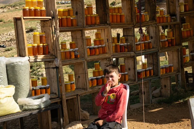 Merchant in Shahre Kord. A young boy selling honey with his family on the empty roads of Shahre Kord. He enjoyed meeting tourists and talking to them, and asked me to take a photo of him once he saw my camera. He then proceeded to make a funny face.