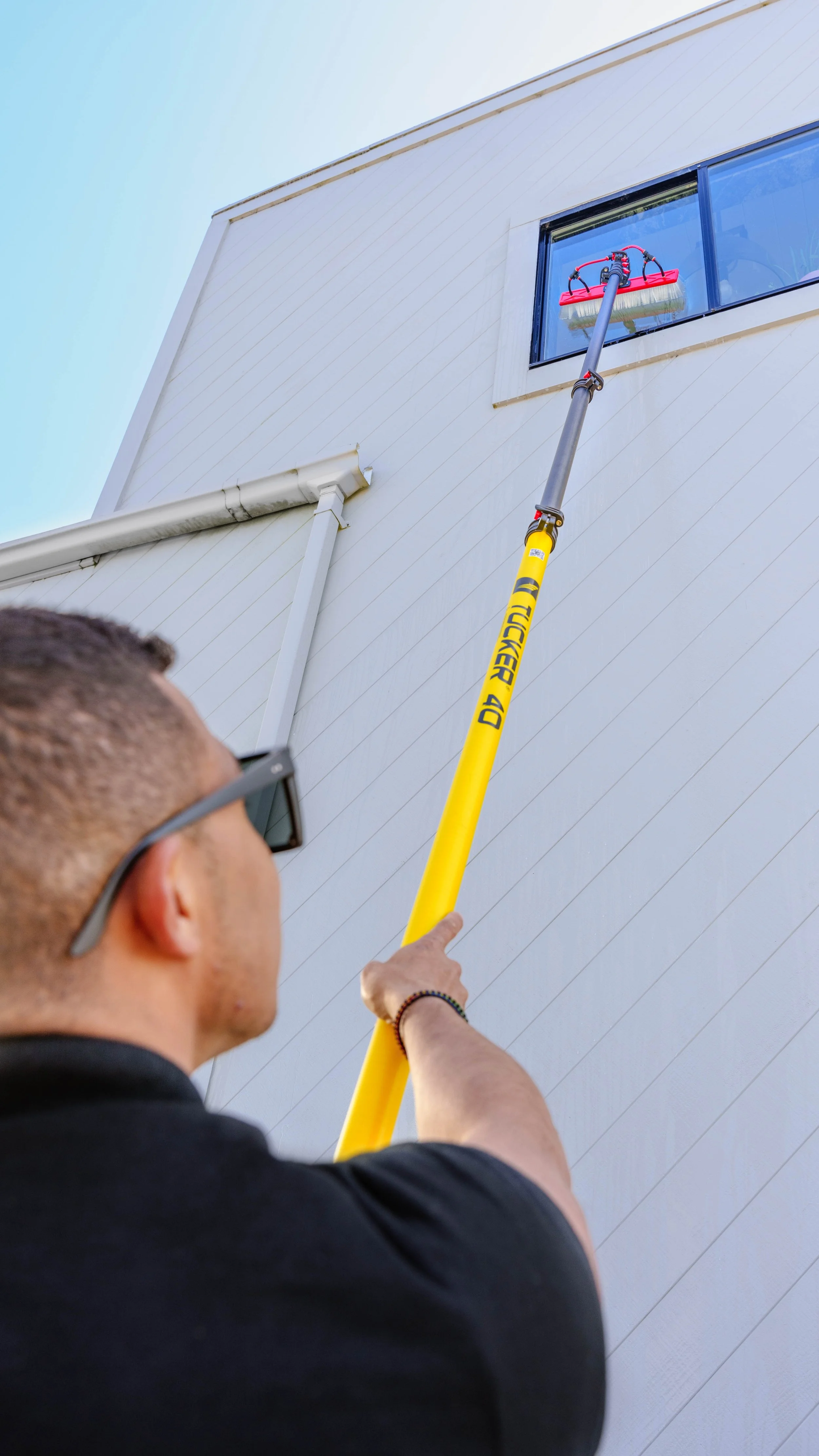 A person cleaning a window on the side of a building using a long pole with a squeegee attachment.
