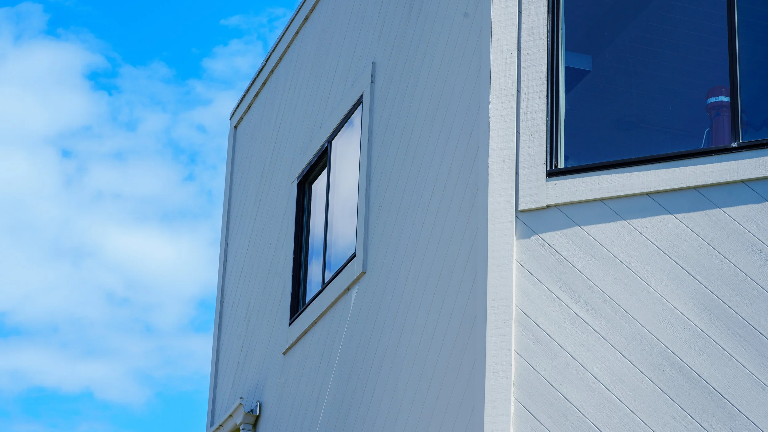 Close-up of the corner of a modern white building with large windows, set against a blue sky with clouds.