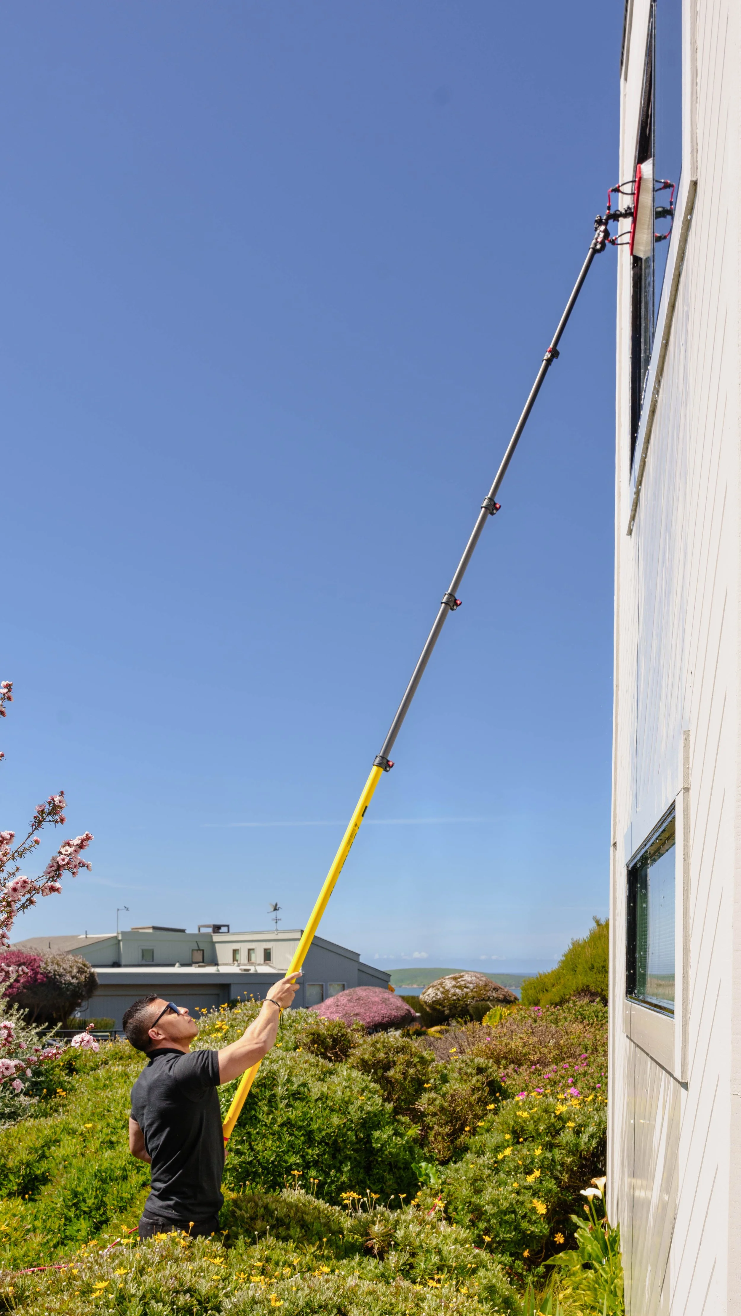 A man using a long tool to clean or perform maintenance on the exterior of a house.