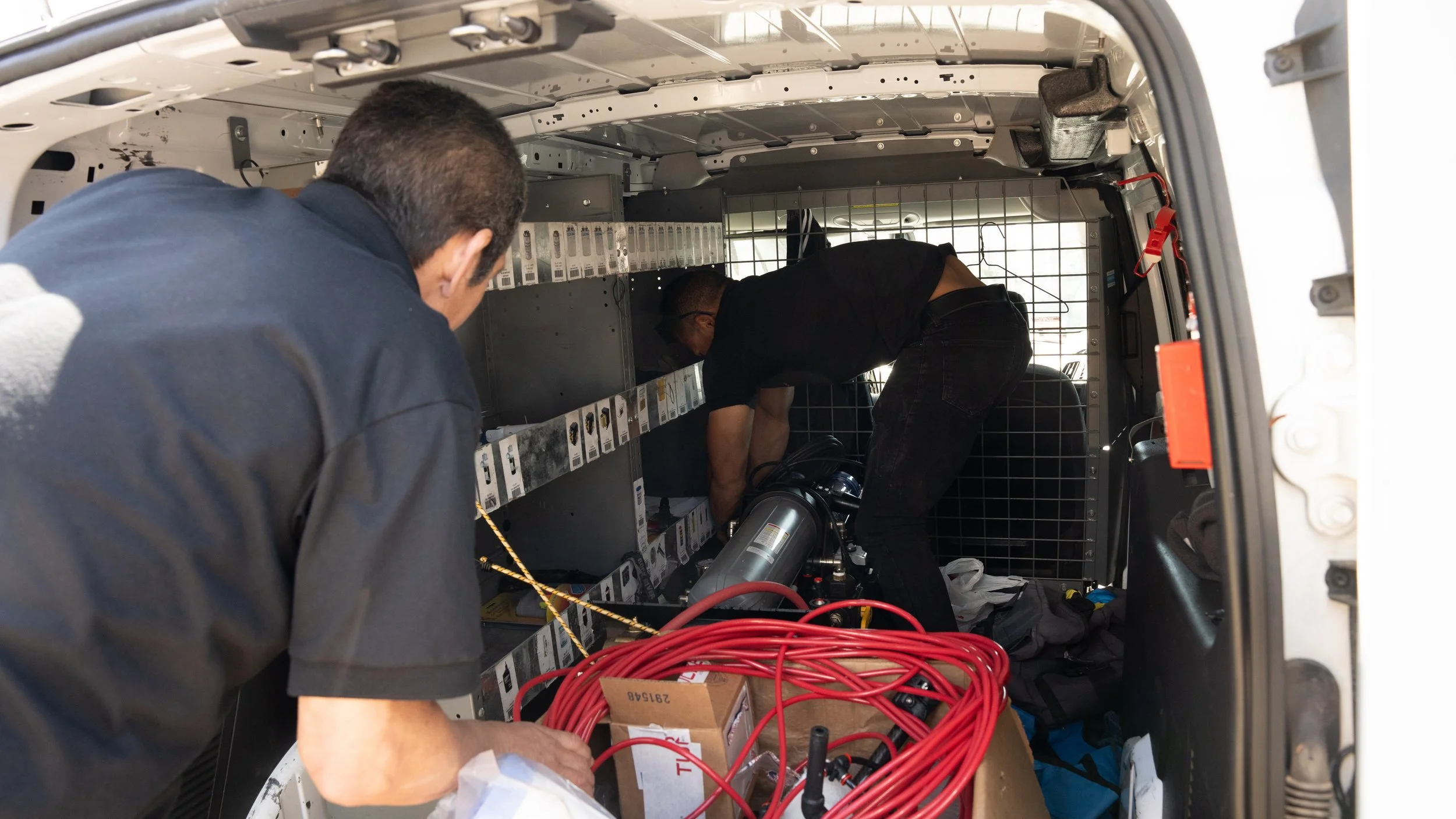 Two technicians working inside an aircraft service panel, surrounded by electronic components and red cables.