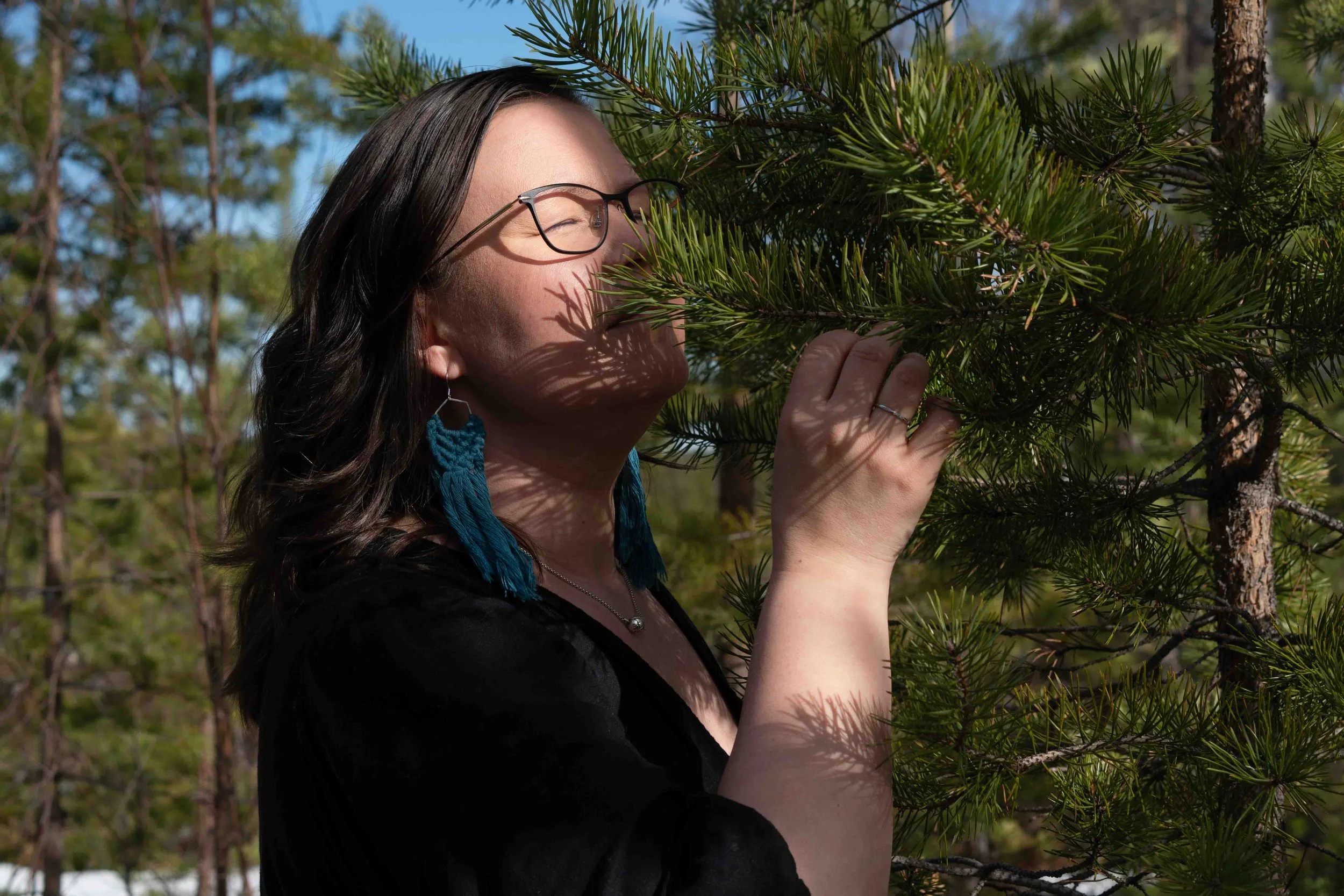 Tummahiuksinen, silmälasipäinen nainen haistelee havunohksia silmät kiinni nautiskellen.