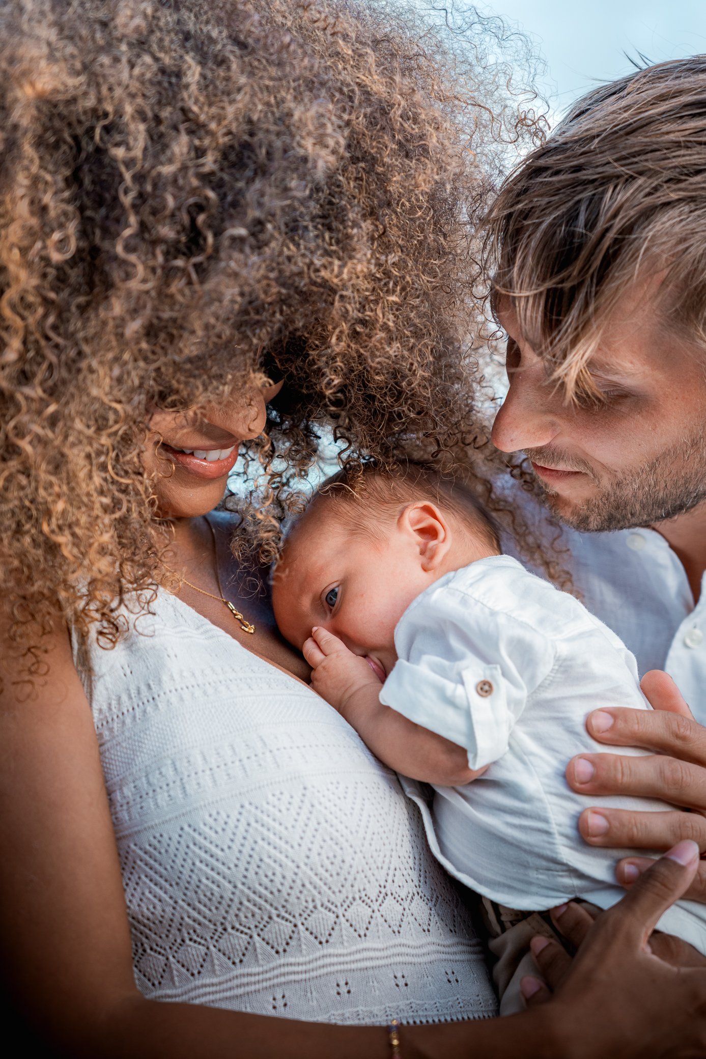 Des parents penchés sur leur nouveau-né, joue contre joue, en tenue blanche