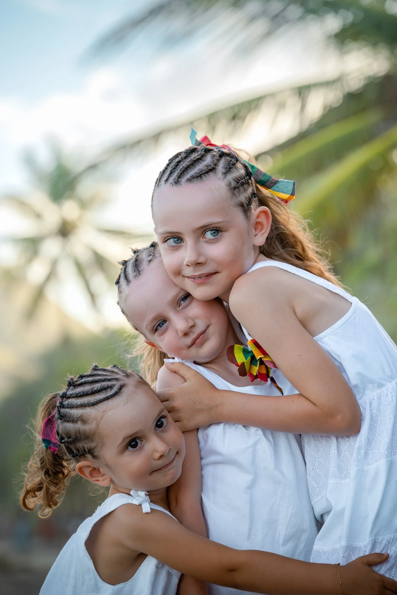 Trois fillettes aux nattes se serrent dans les bras, un ruban coloré dans les cheveux