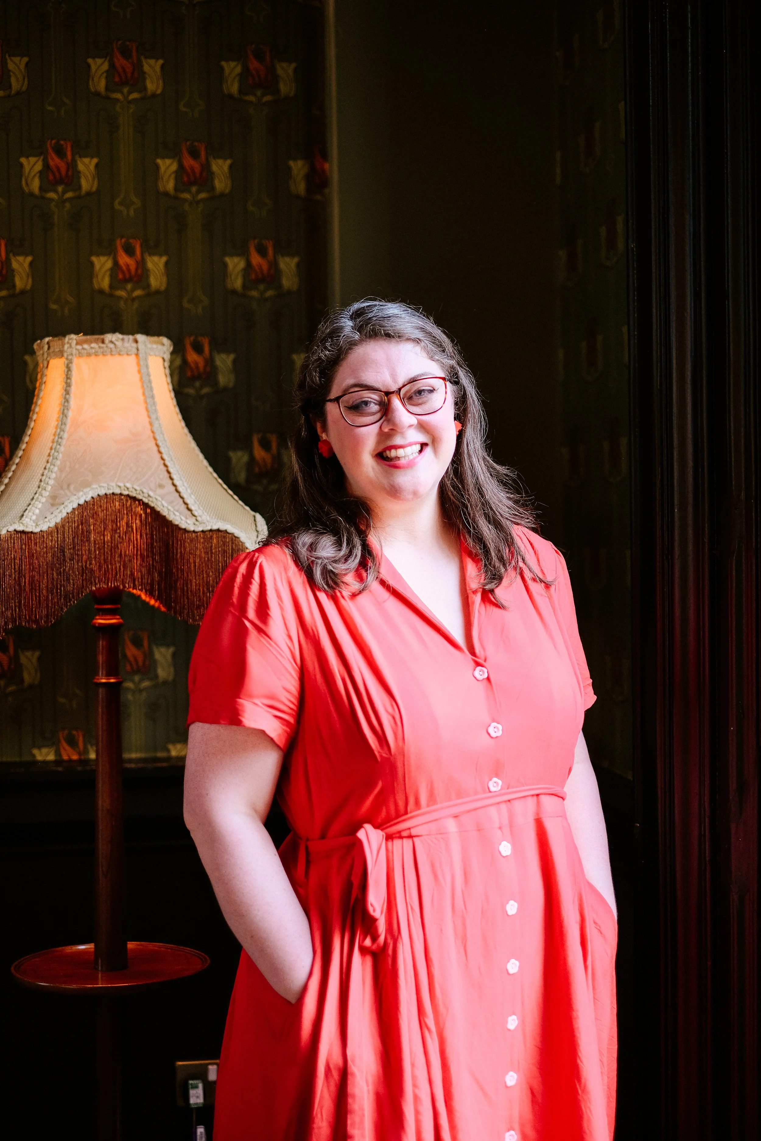 Laura, a woman wearing a red dress, stands in front of patterned wallpaper