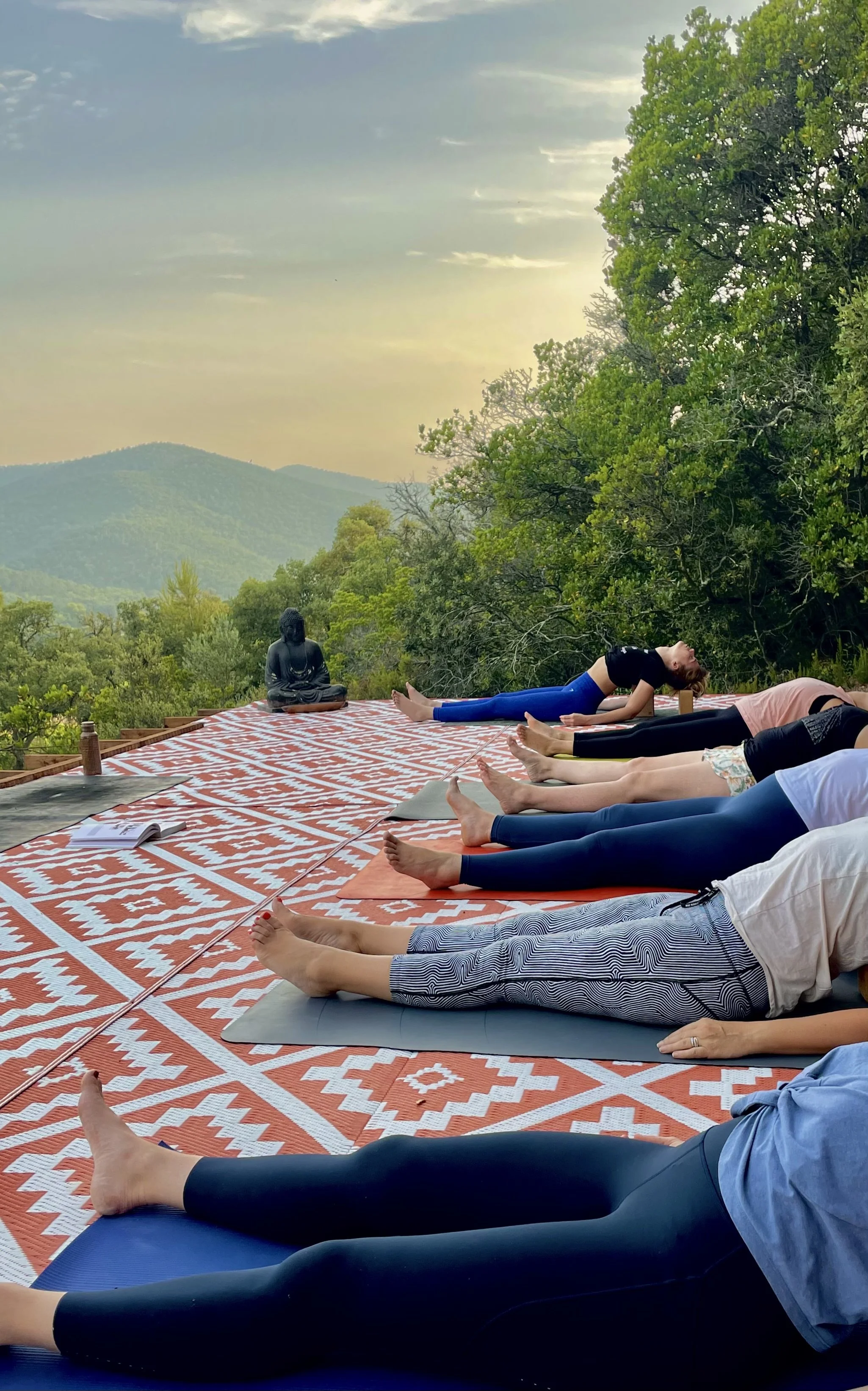 Terrasse de yoga en plein air à Origins Yoga, accueillant des séances collectives au cœur de la nature. Les participants pratiquent dans un cadre calme et arboré, avec vue sur les collines et une atmosphère propice à la concentration, au ressourcemen