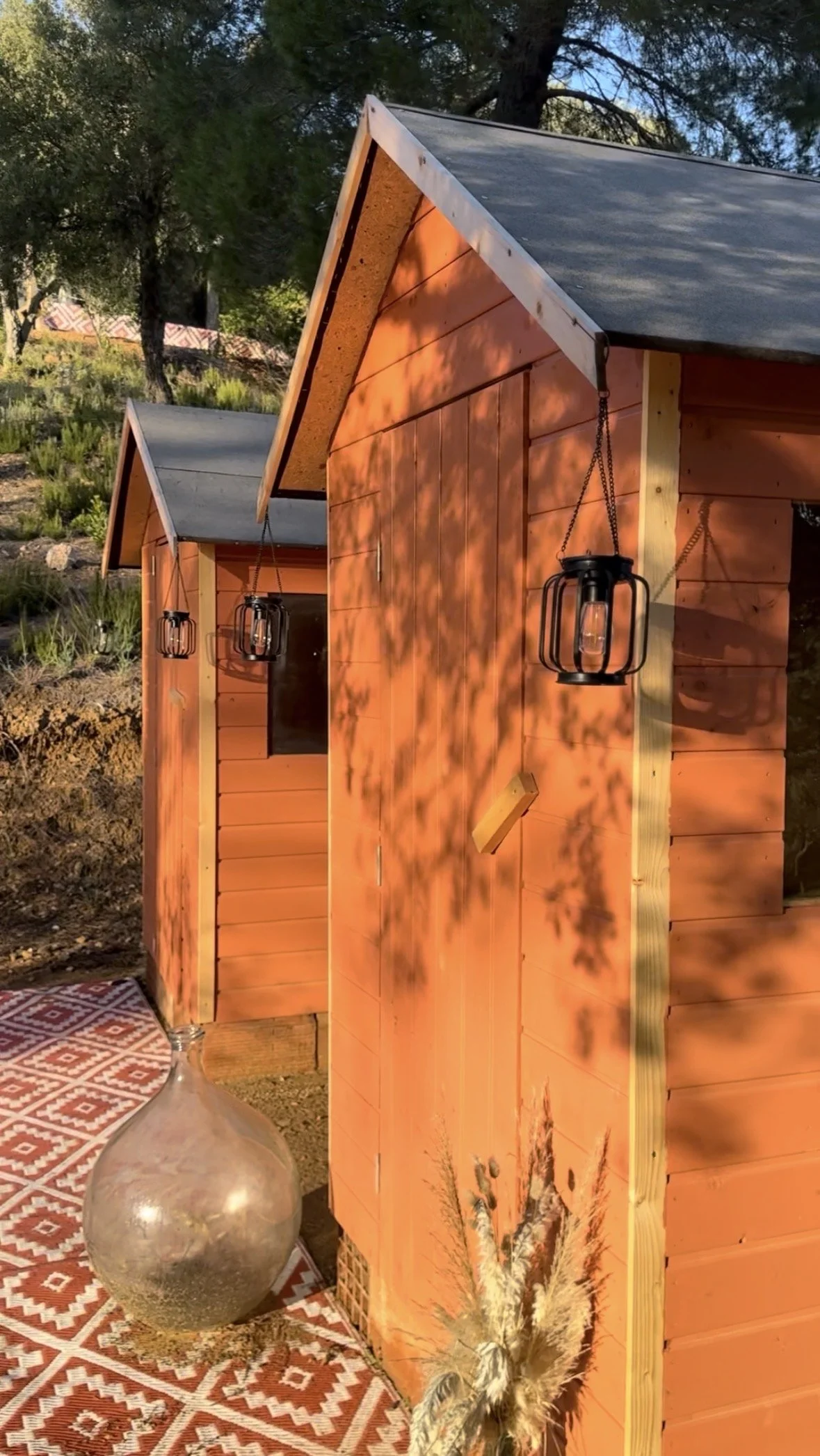Toilettes sèches extérieures en bois aux teintes ocre, intégrées dans la nature et pensées comme de véritables petits espaces soignés, à la fois esthétiques et fonctionnels.