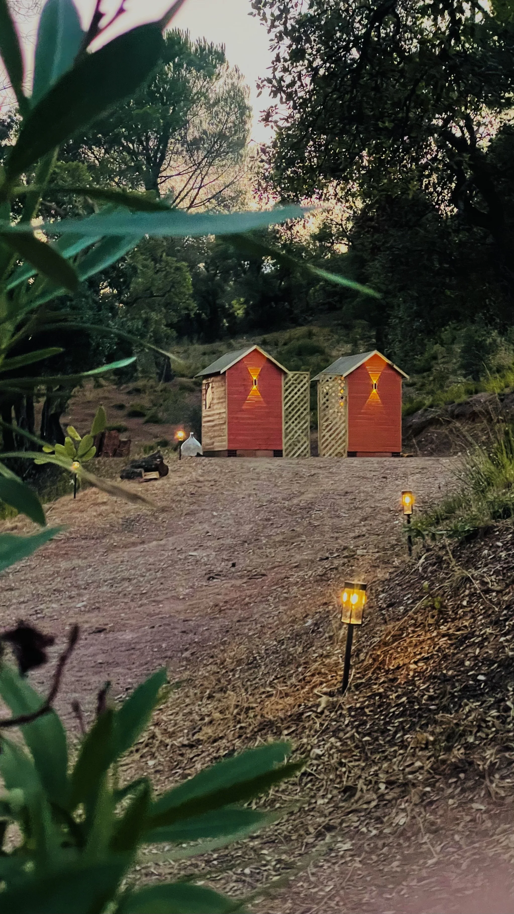 Chemin menant aux toilettes sèches, volontairement situé à distance des espaces de vie, bordé de végétation et éclairé par des lumières solaires pour un accès confortable de jour comme de nuit.