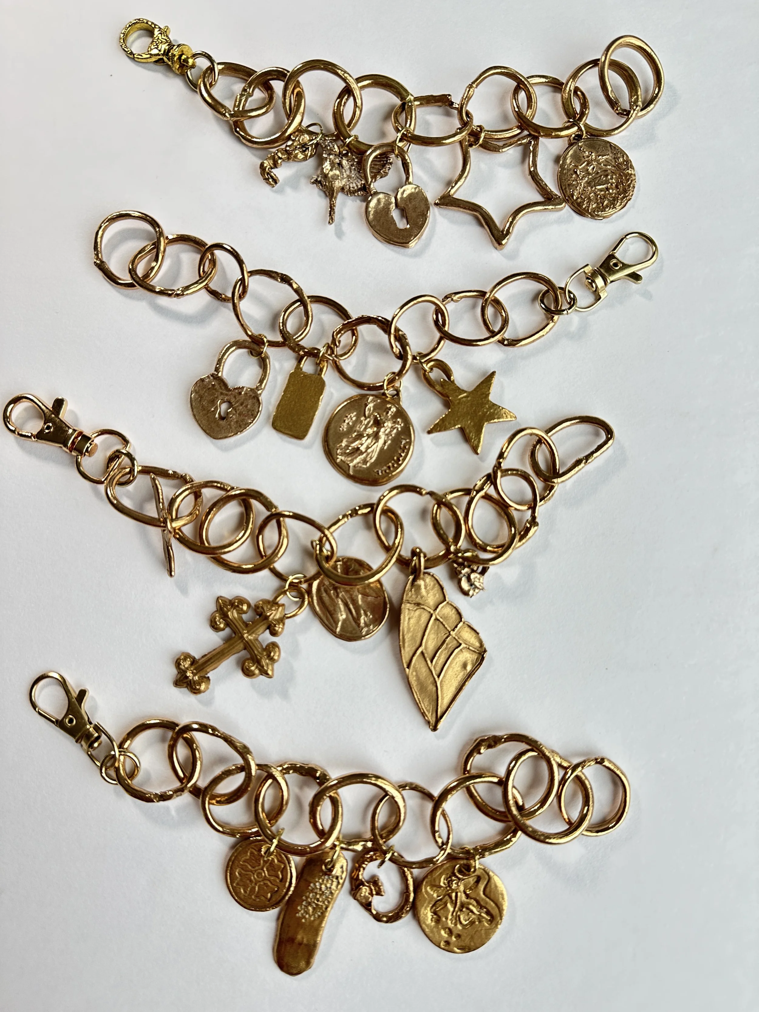 Four gold charm bracelets with various charms including a cross, star, heart, coin, and other shapes, placed on a white background.