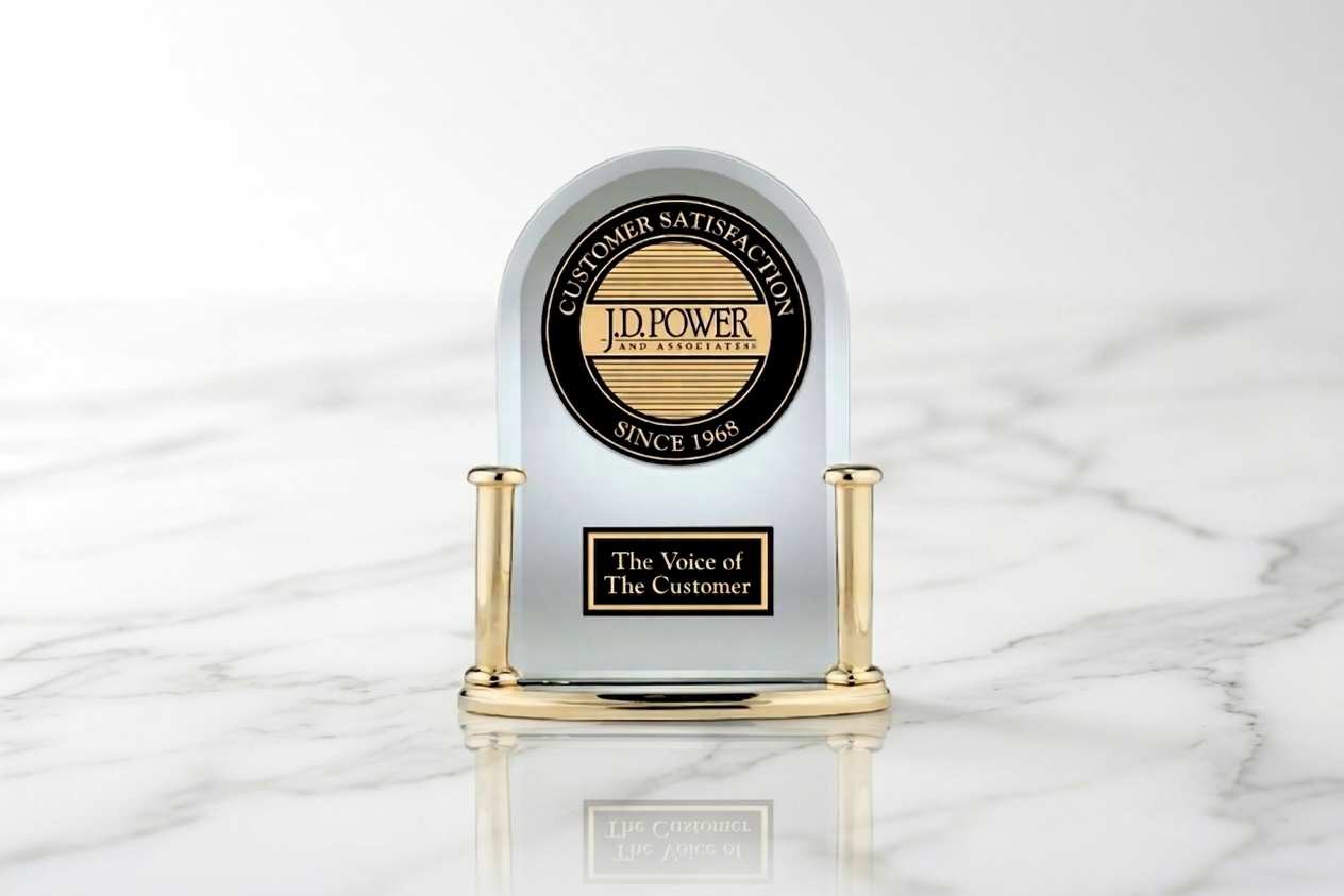 A decorative trophy with a black and gold emblem reading "Customer Satisfaction Since 1968" and "J.D. Power and Associates." The trophy also features a black plaque with the inscription "The Voice of The Customer." It is placed on a white marble surface.