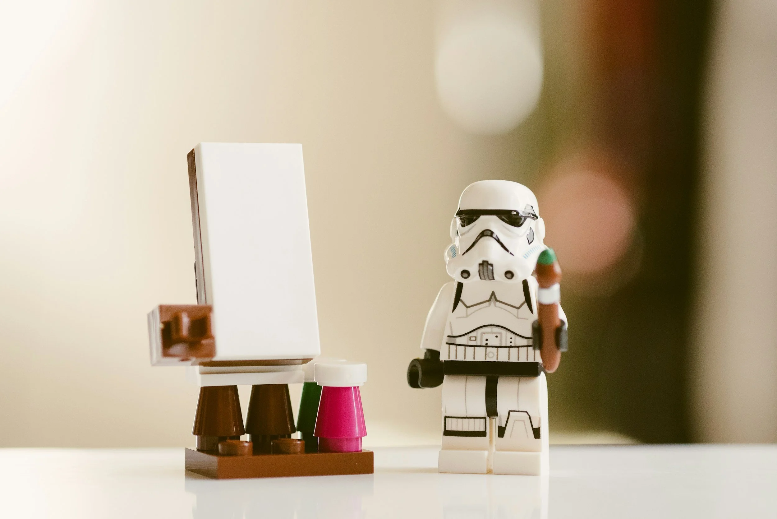 Lego stormtrooper holding a paintbrush next to an easel.