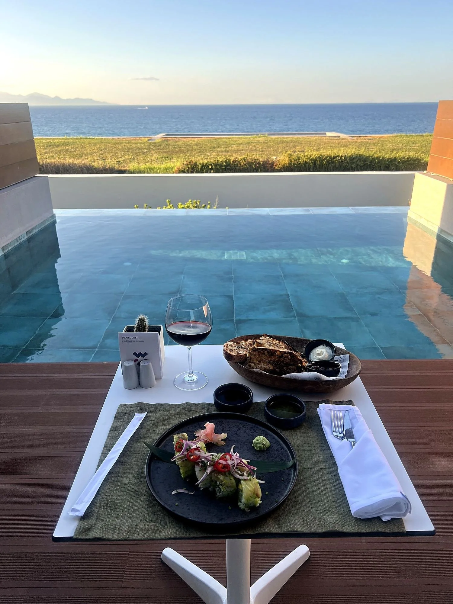 Image of my dinner from my private terrace and plunge pool overlooking the Ionian Sea, bread with tzatziki and sushi and a glass of red wine.