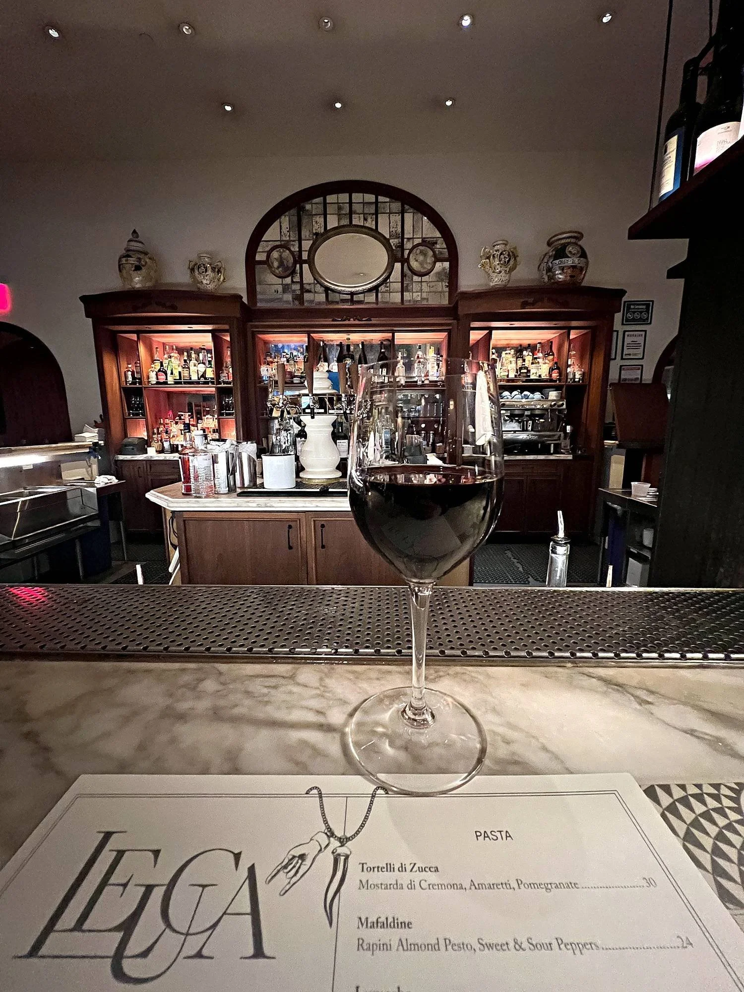 A glass of red wine and the menu at the marble bar of Leuca, the restaurant at The William Vale in Brooklyn.