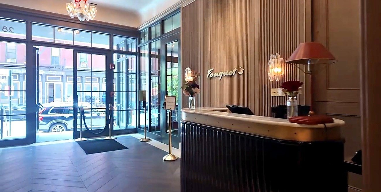 The front desk at Fouquet's New York in Tribeca, with the Fouquet's sign on the wood wall behind it and the street doors to the left.